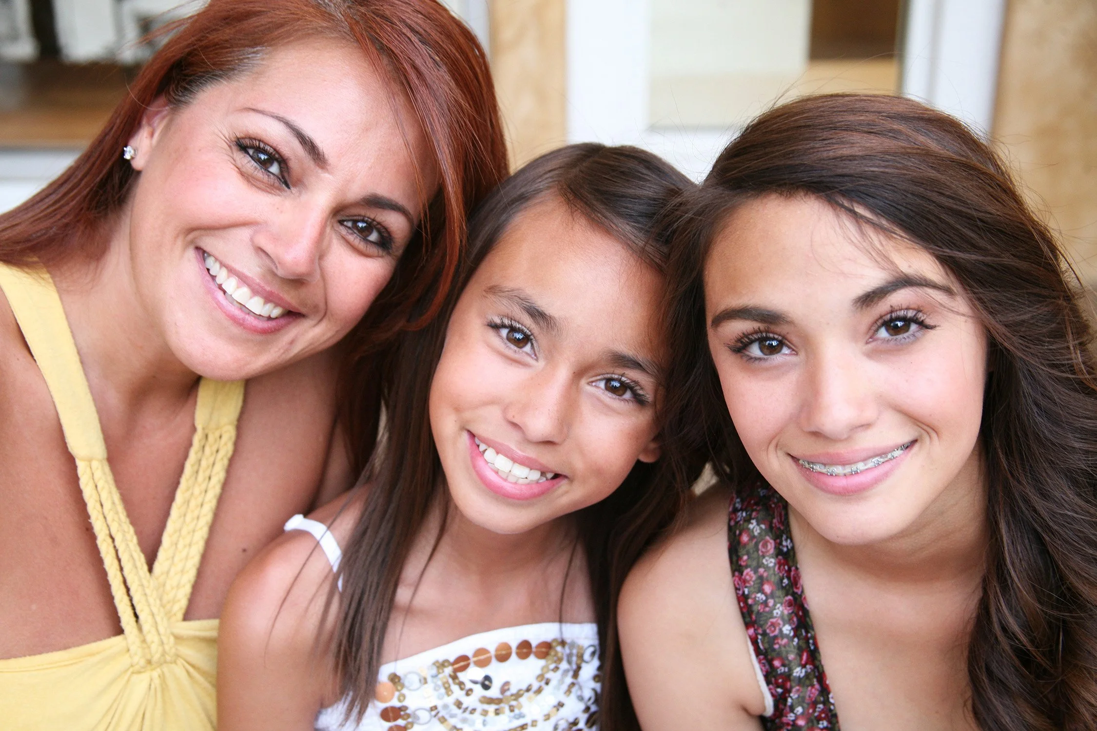 A close up of a family of three, a mom and two girls smiling at the camera.