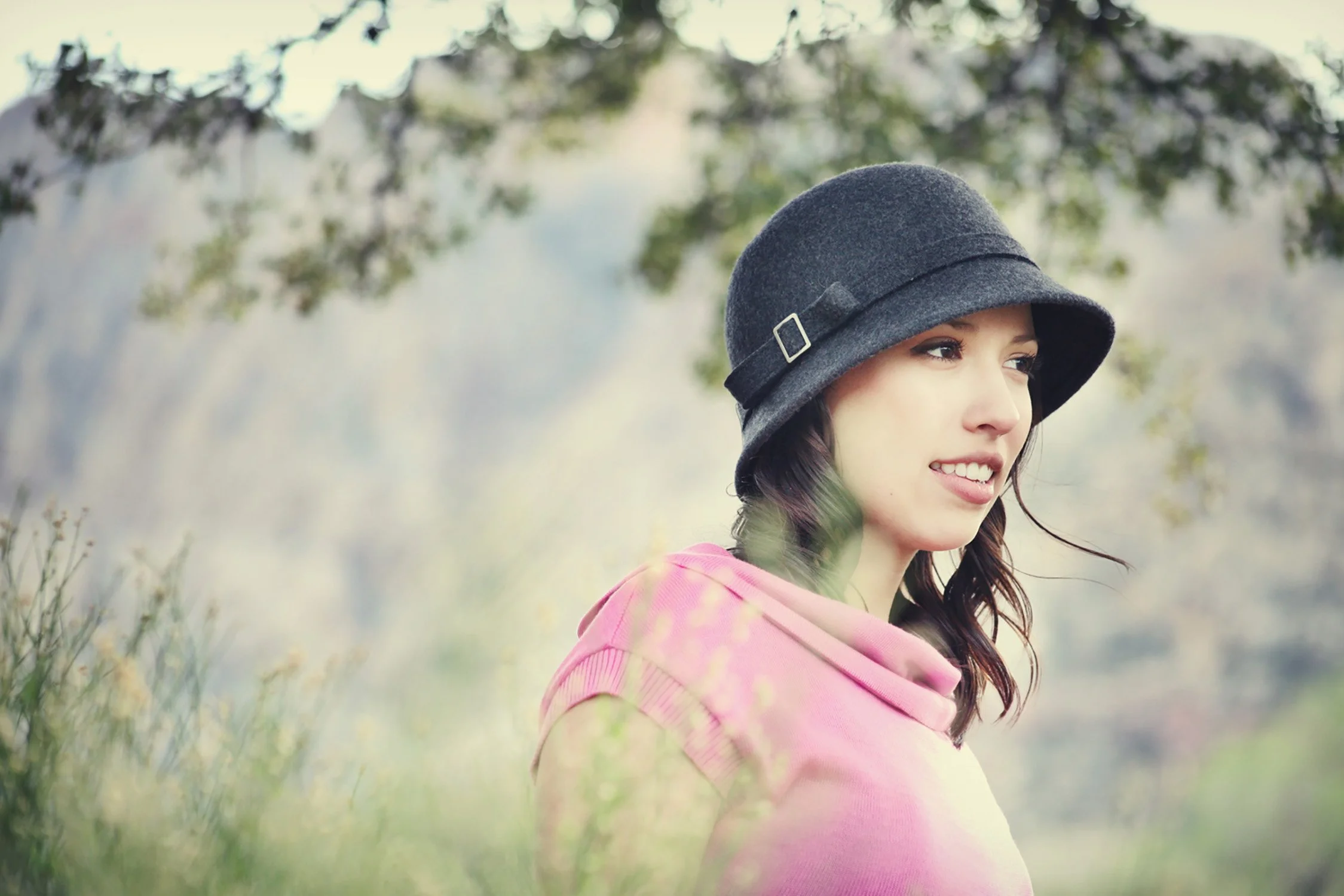 a high school senior is looking away from the camera, standing around trees and bushes in an up close shot. You can also see the mountains in the background