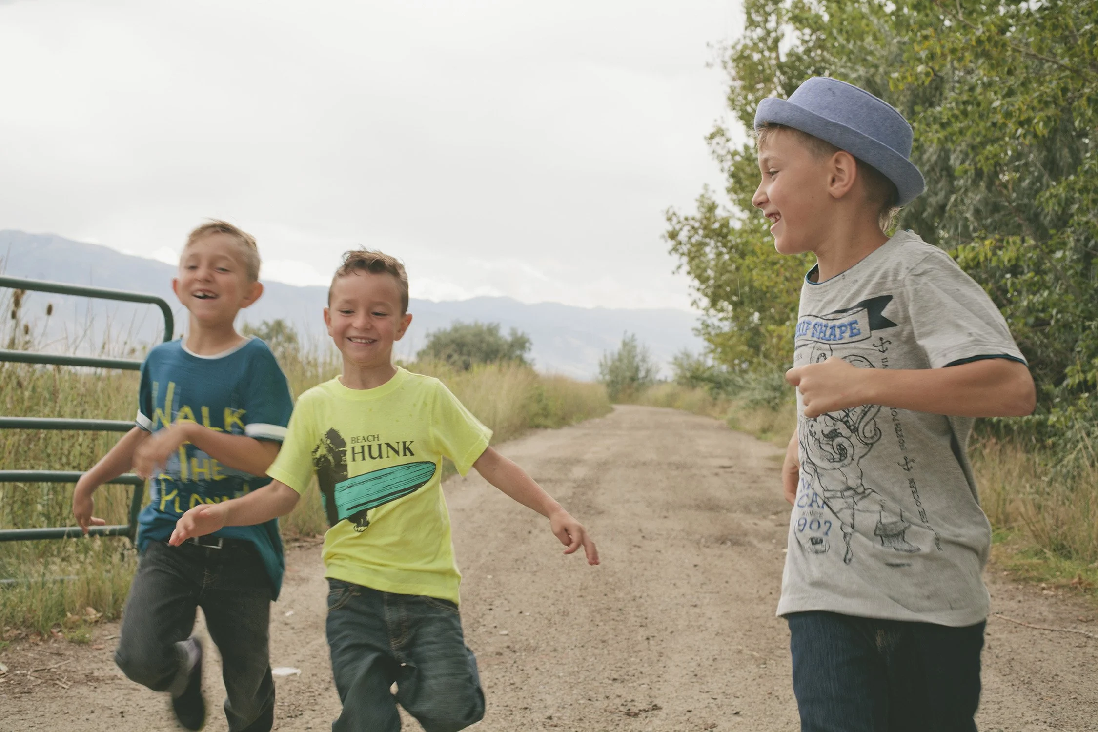 three young brothers age ranging from 7 to10 years old are running on a dirt road towards the camera, laughing and looking at each other