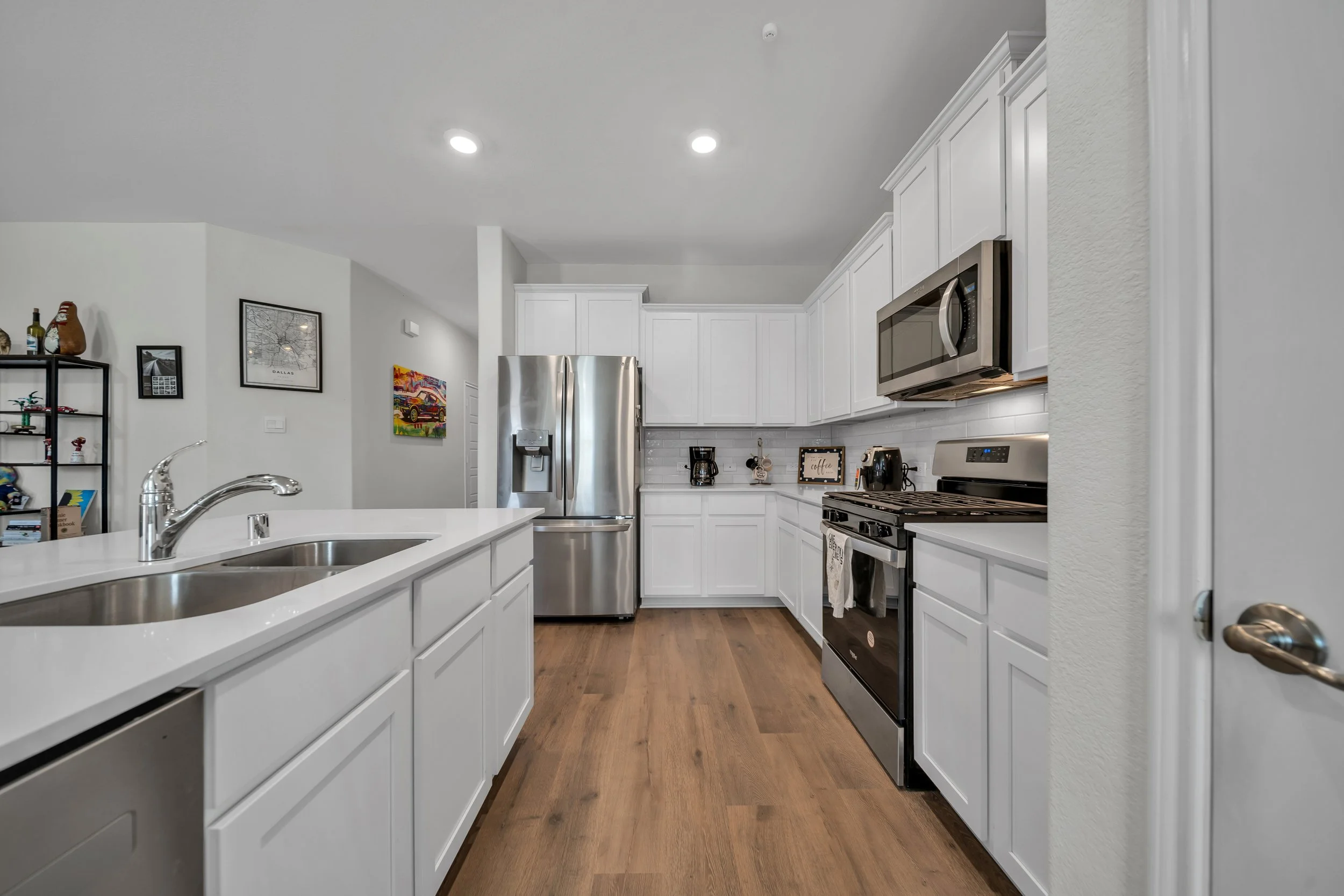Modern kitchen with white cabinets, stainless steel appliances, and wood flooring.