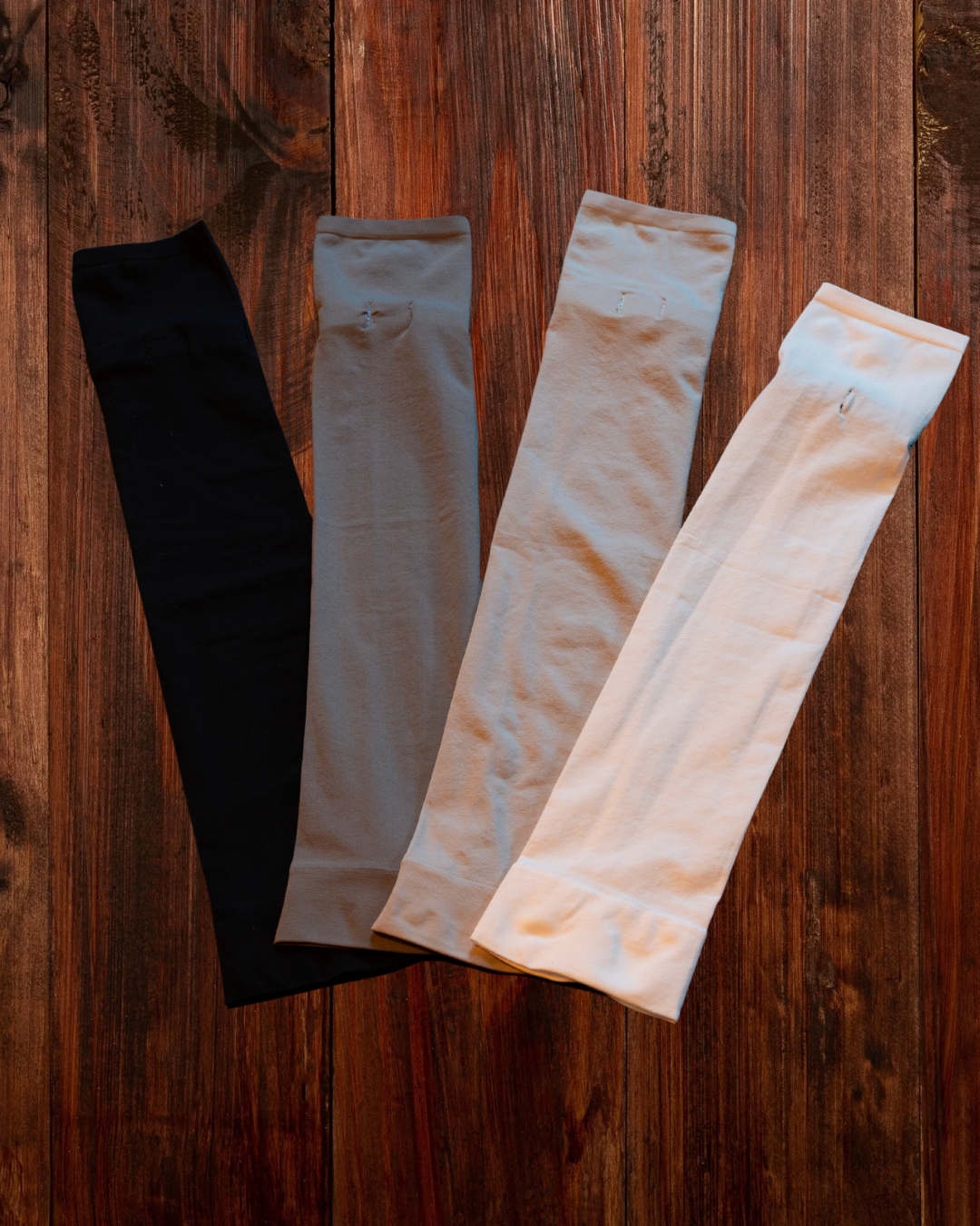 Four folded fabric pieces in black, gray, beige, and white on a wooden surface.
