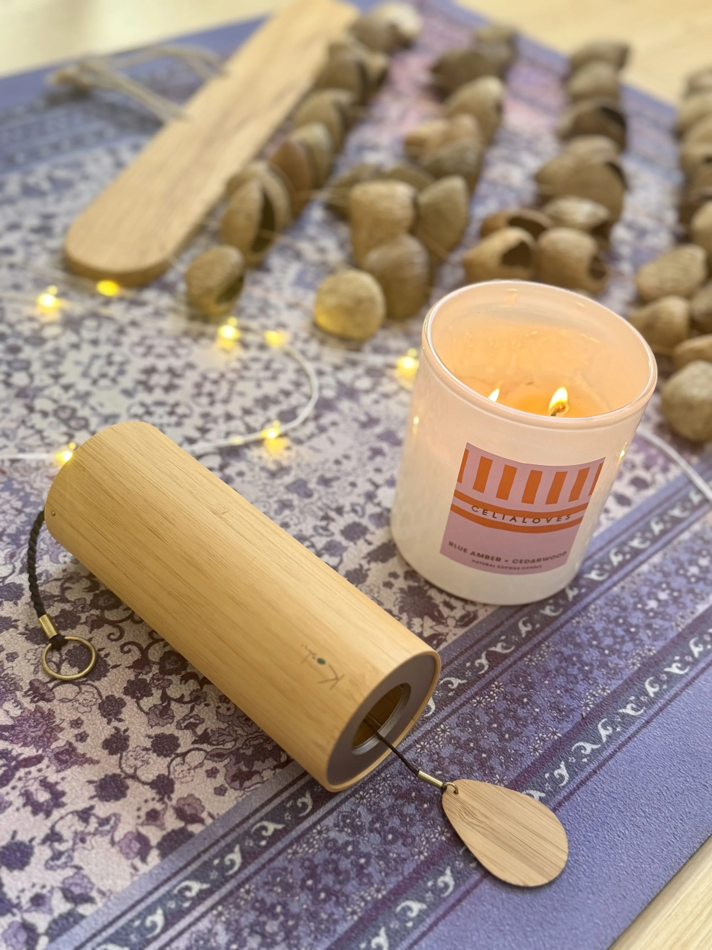 Candle and wooden prayer wheel on a patterned tablecloth surrounded by walnuts and string lights.