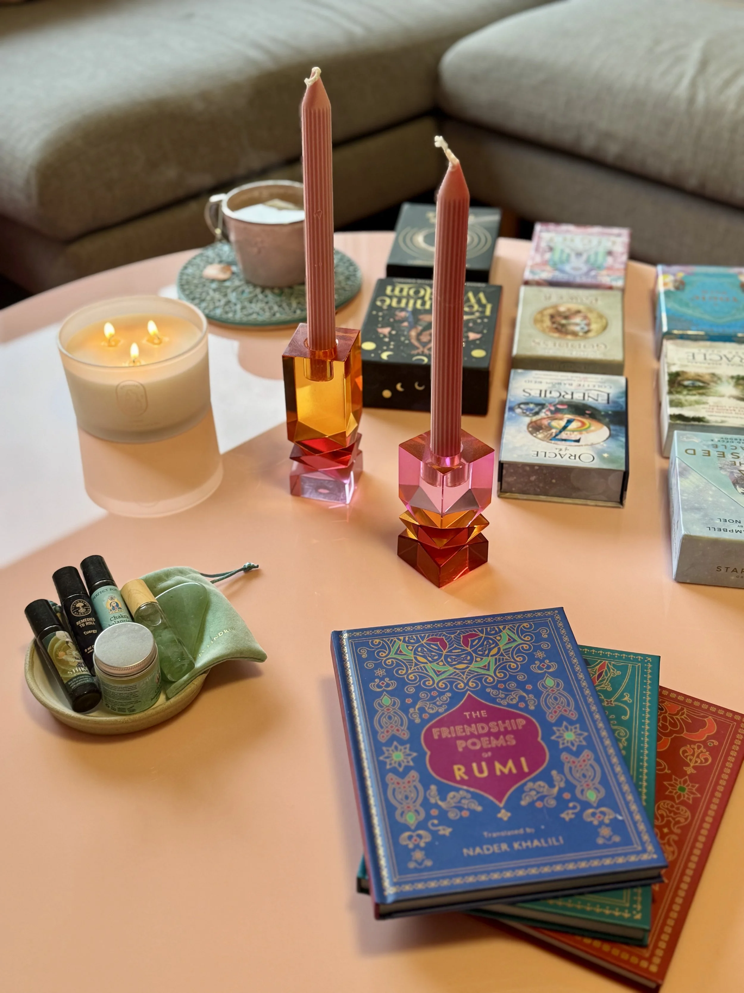 A pink round table with candles, Tarot cards, a candle, and essential oils, with a beige couch in the background.