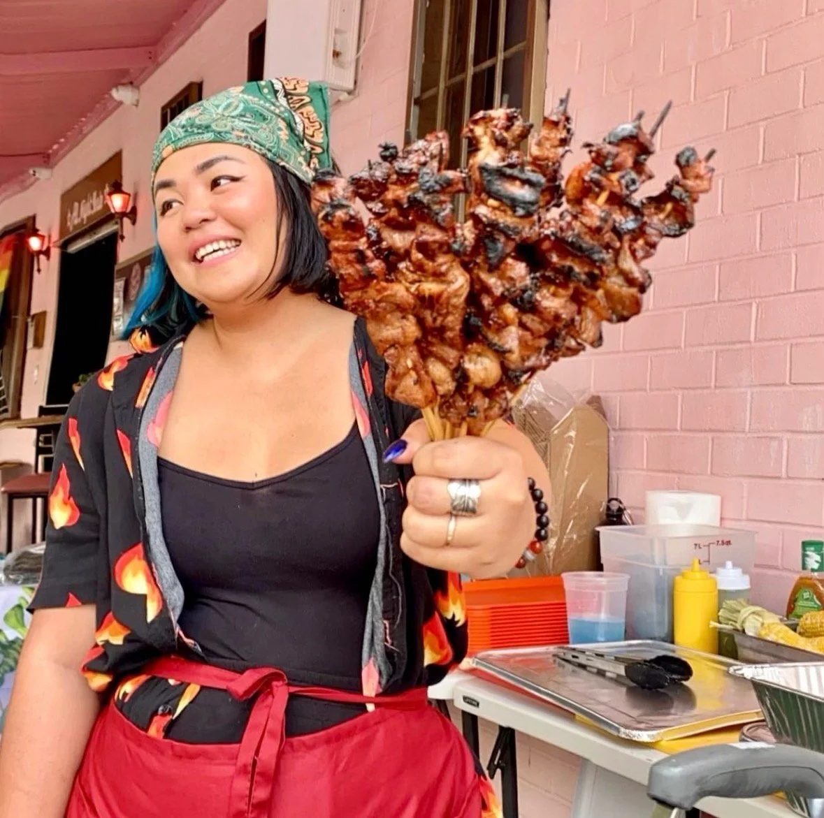 photo of a woman in black and red ensemble, holding filipino pork bbq sticks
