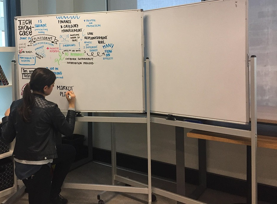 Person writing on a whiteboard with notes and diagrams at a tech showcase event.
