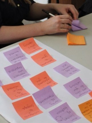 Person writing on sticky notes at a desk covered with colorful sticky notes arranged on paper.