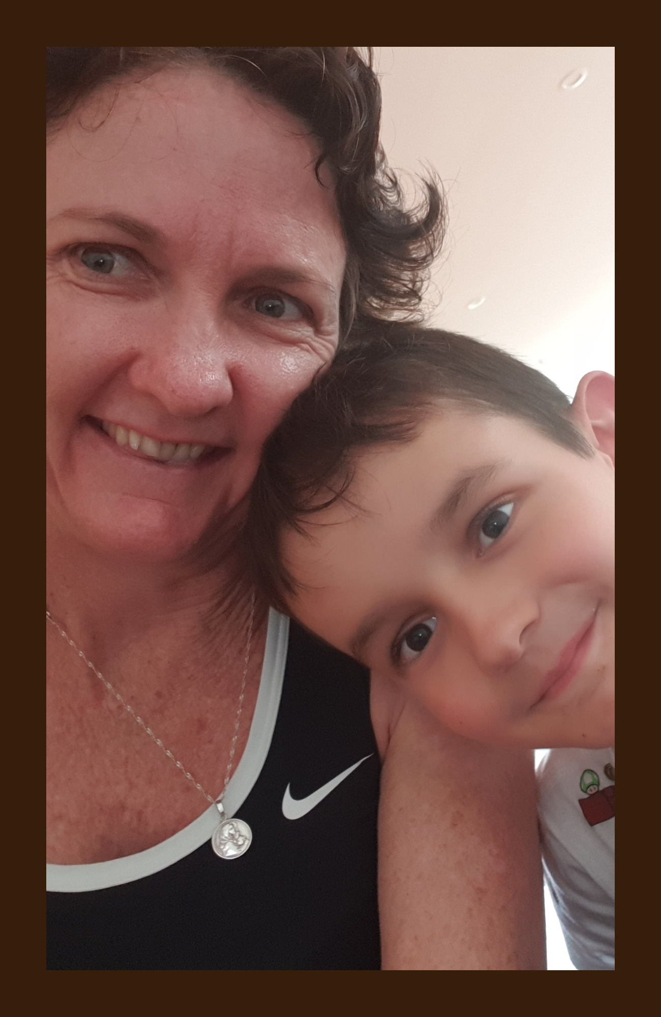 A woman and a young boy taking a close-up selfie together, smiling and showing a friendly moment.