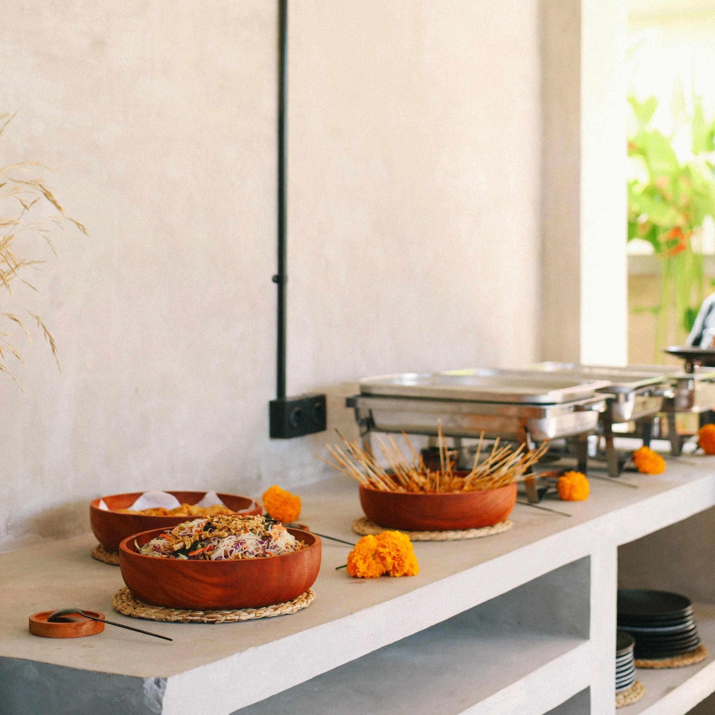 A display of fresh  food on a table. The dishes include various colorful salads and condiments in terracotta bowls, with some marigold flowers as decoration.