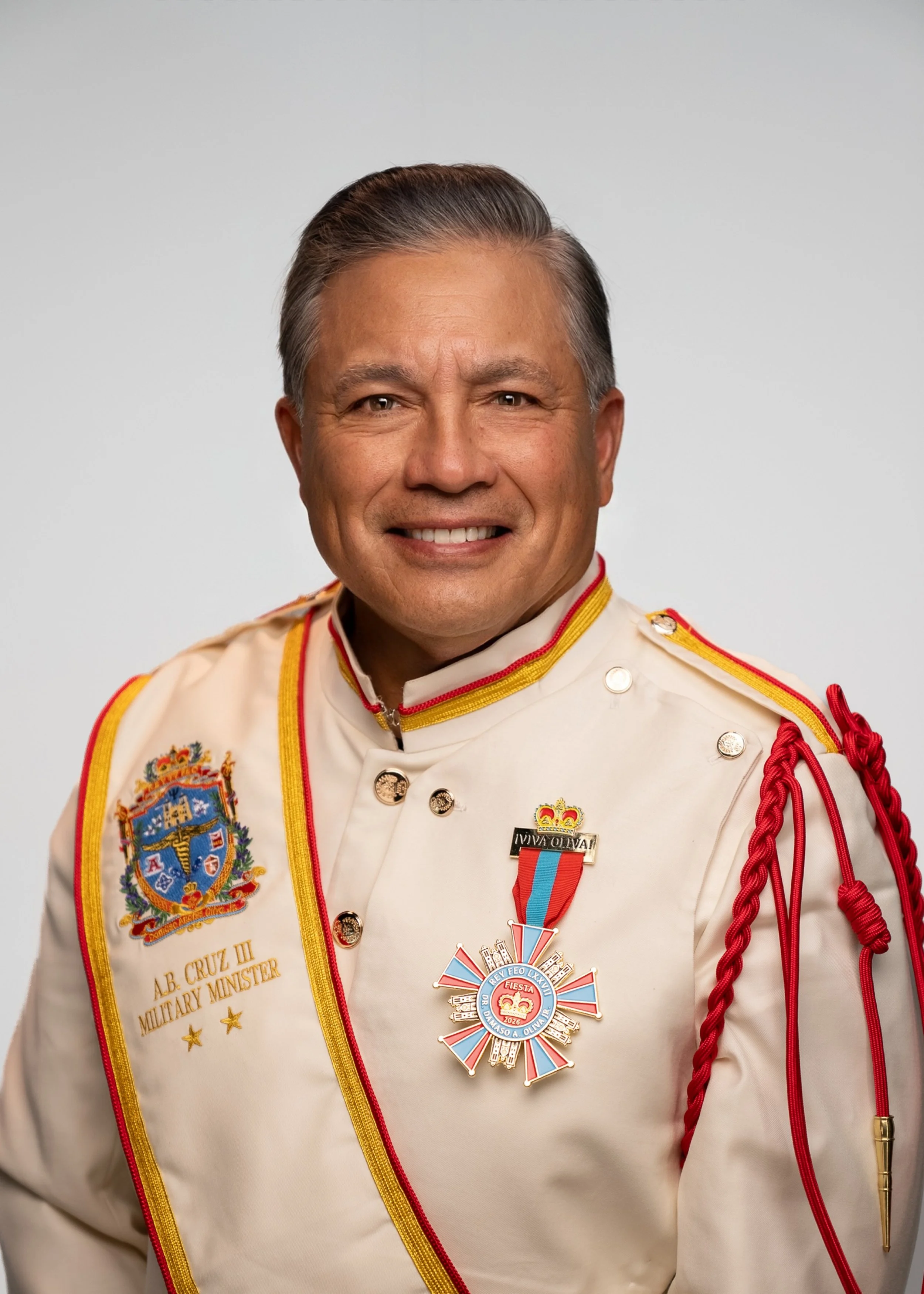 A smiling man with dark hair slicked back, wearing a red button-up shirt, against a plain light gray background.