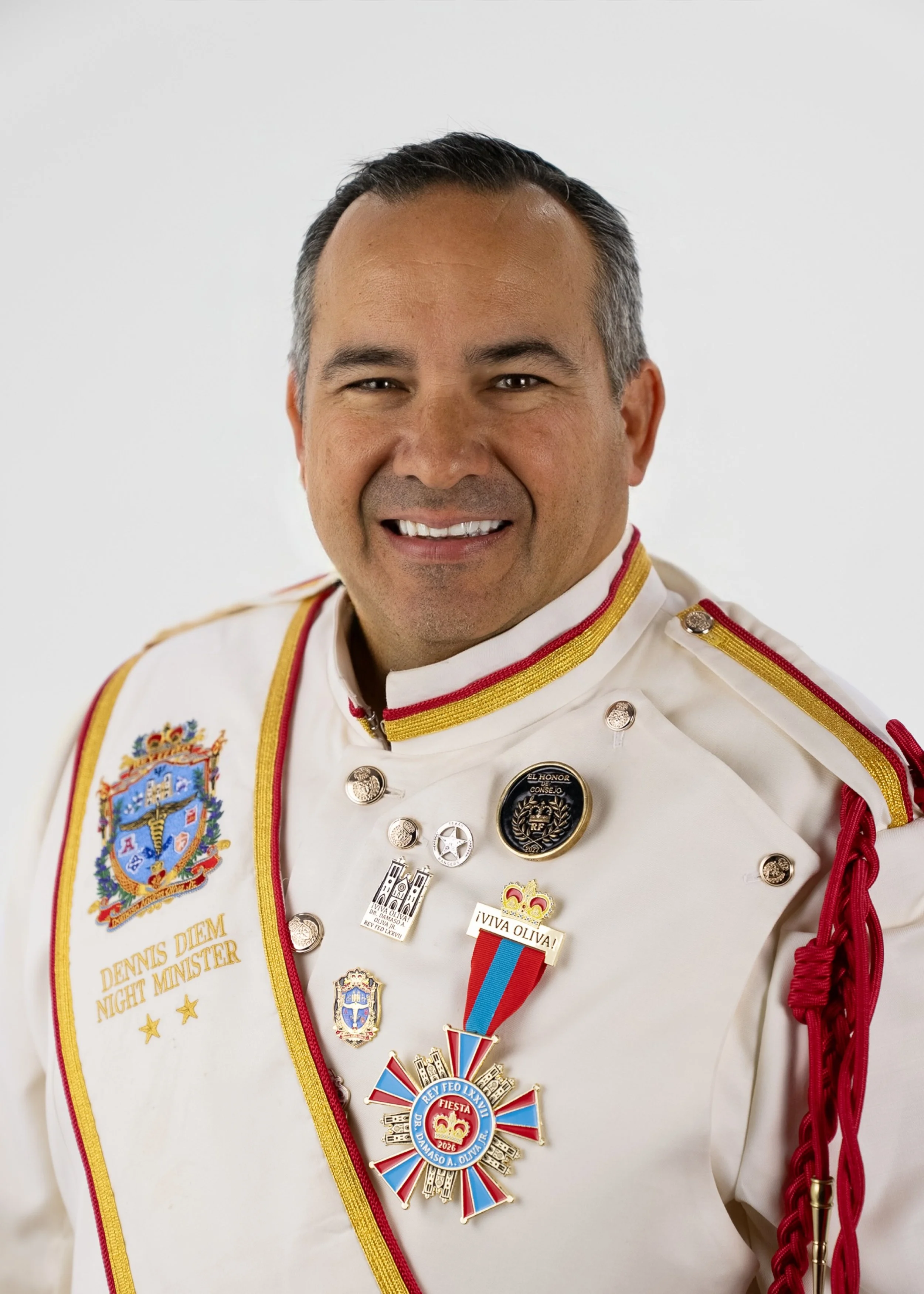 A middle-aged man smiling, wearing a bright red shirt, against a plain light gray background.