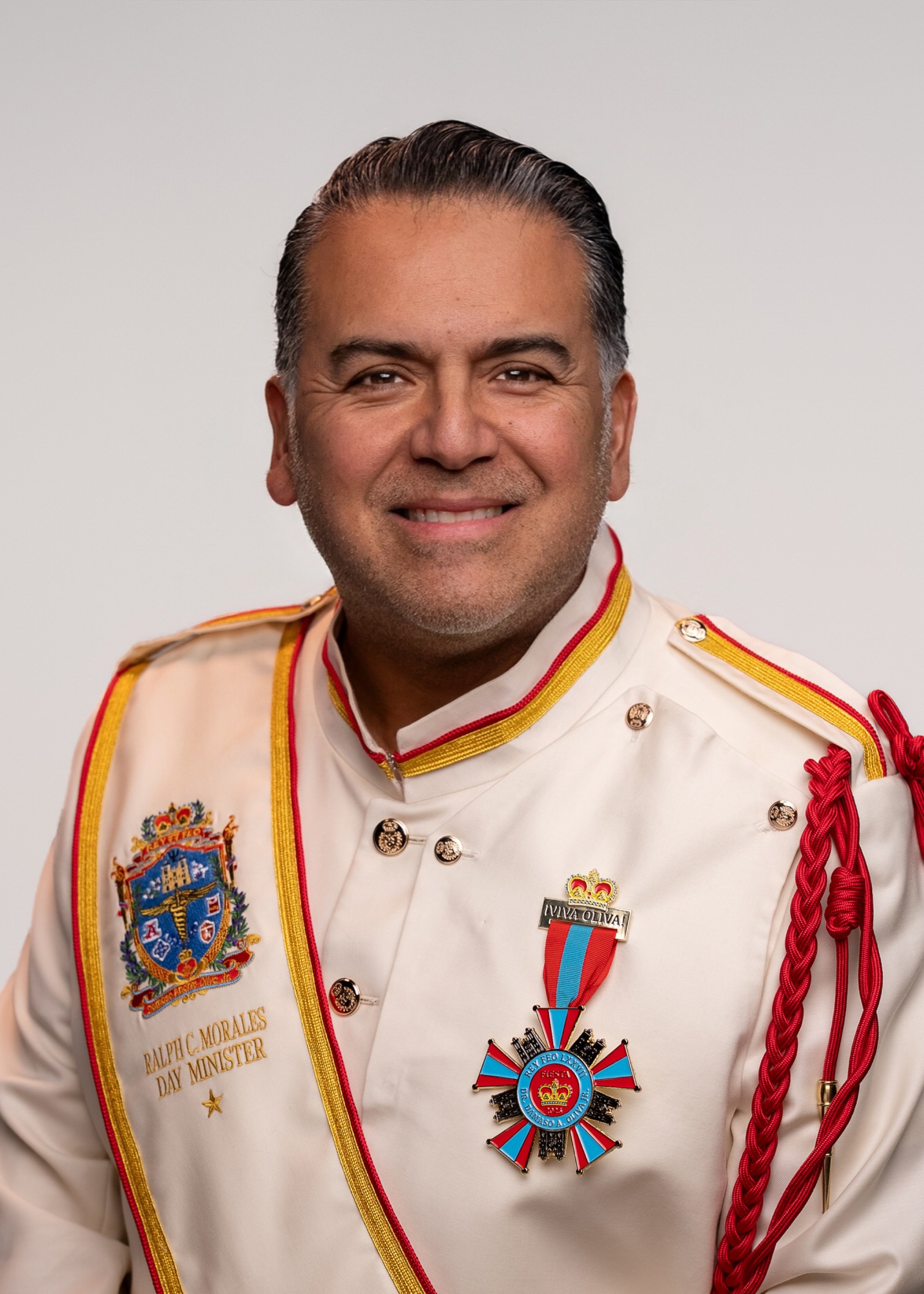 A smiling man with gray hair and a beard, wearing a red button-up shirt, posed against a plain light gray background.