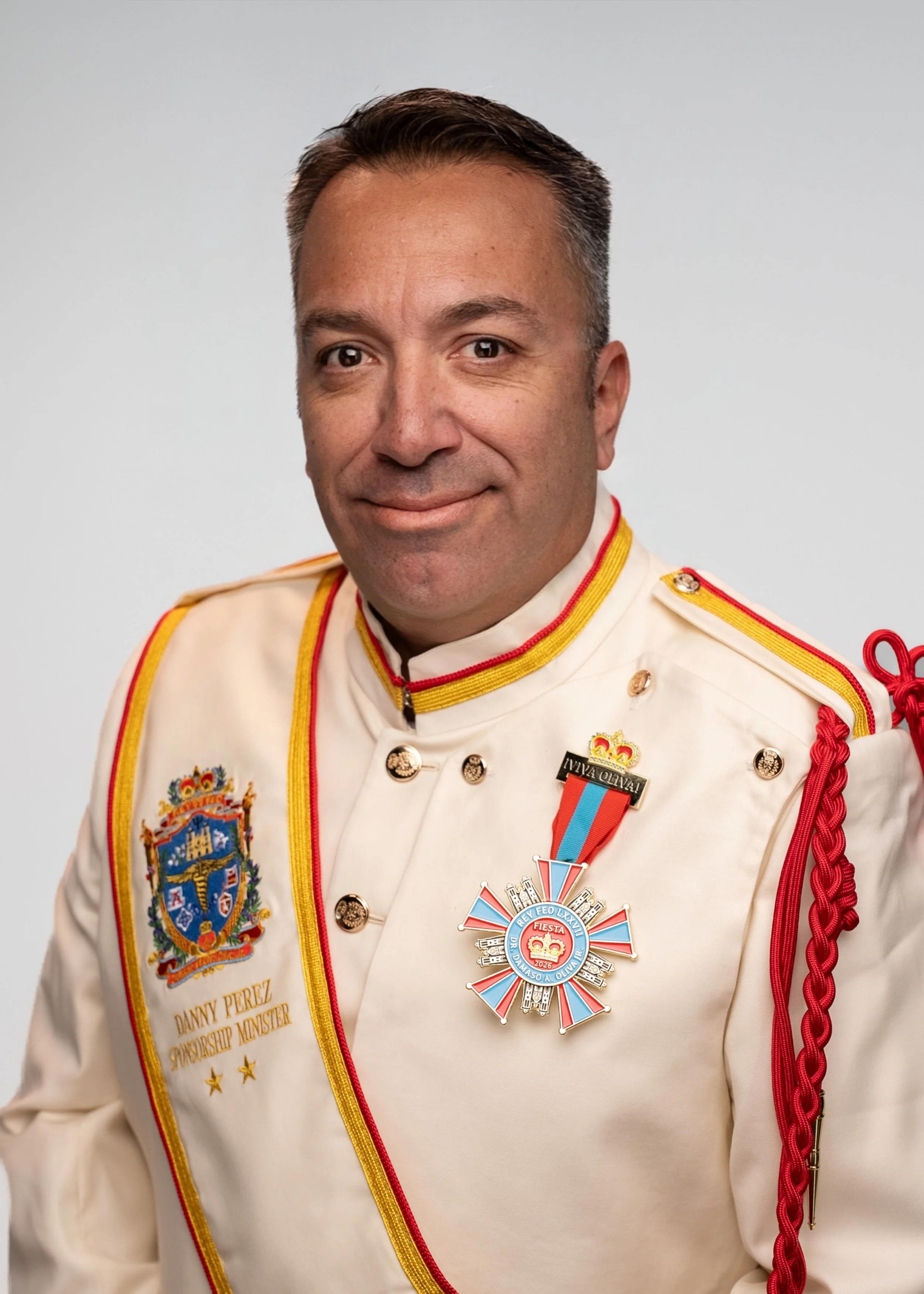 A man in a red collared shirt smiling against a plain, light gray background.