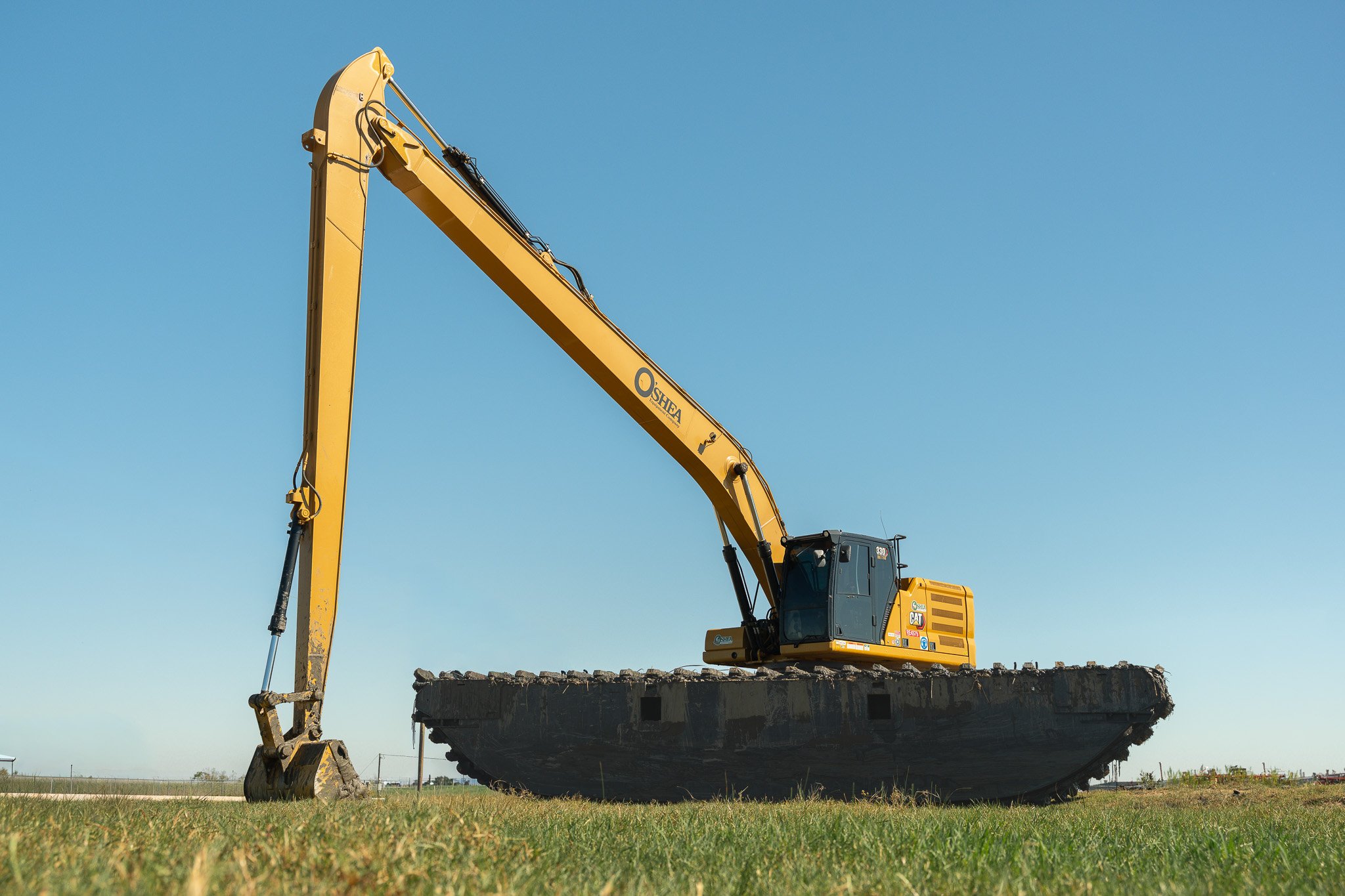 A yellow excavator with a black cab is working on a construction site with a clear blue sky in the background.
