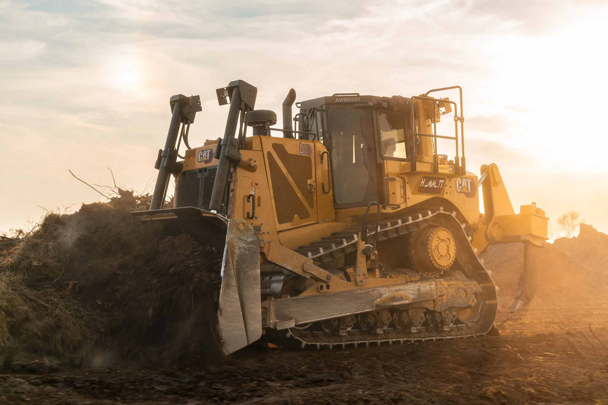 A yellow Caterpillar bulldozer moving dirt during sunset.
