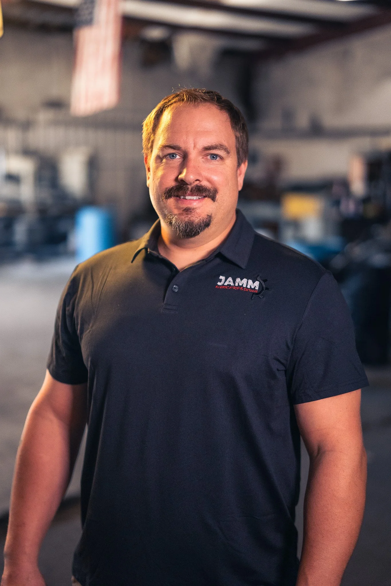 Man in black polo shirt with 'JAMM' logo standing in industrial setting.