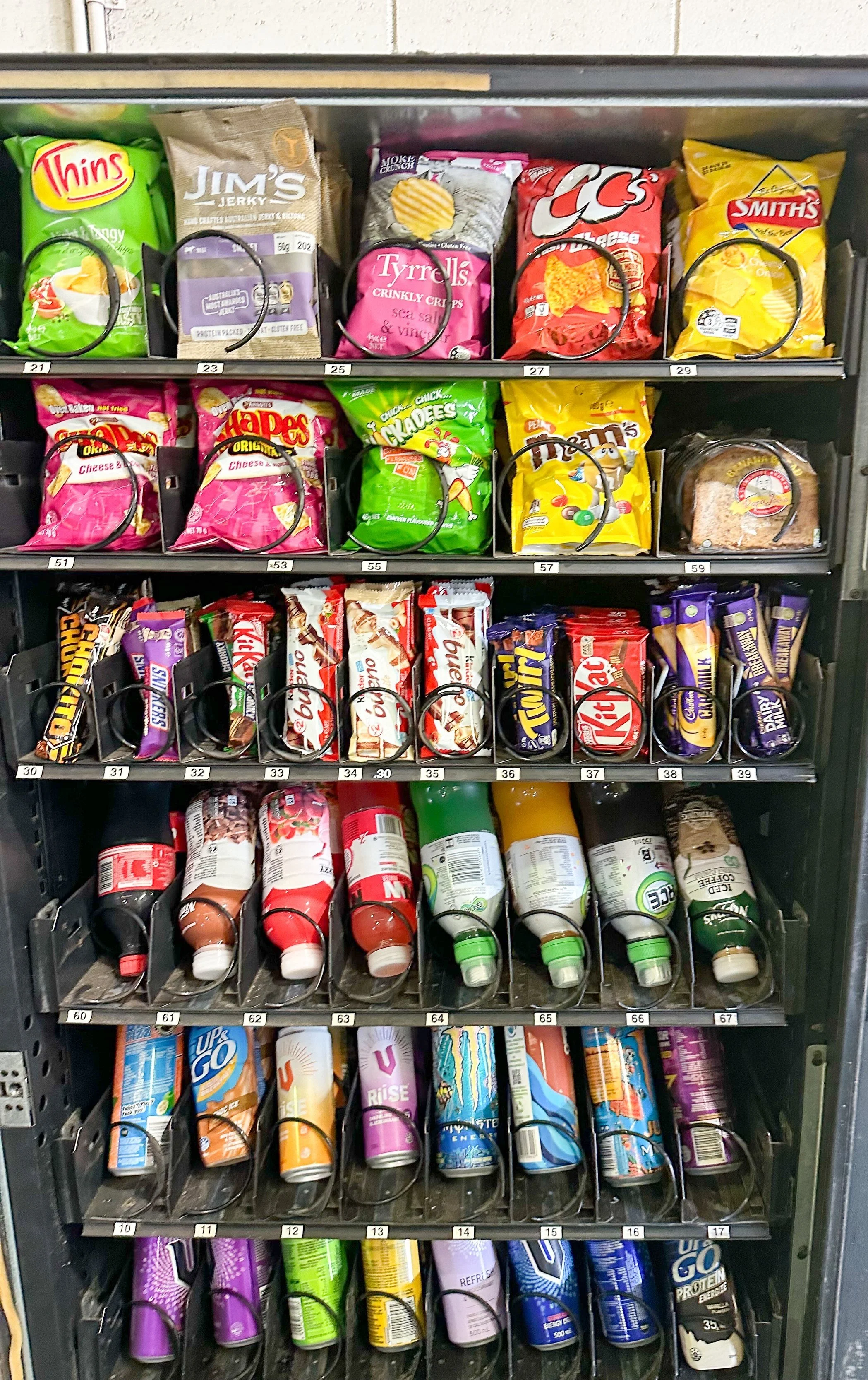 Vending machine with chips, candy bars, snacks, and beverages on various shelves.