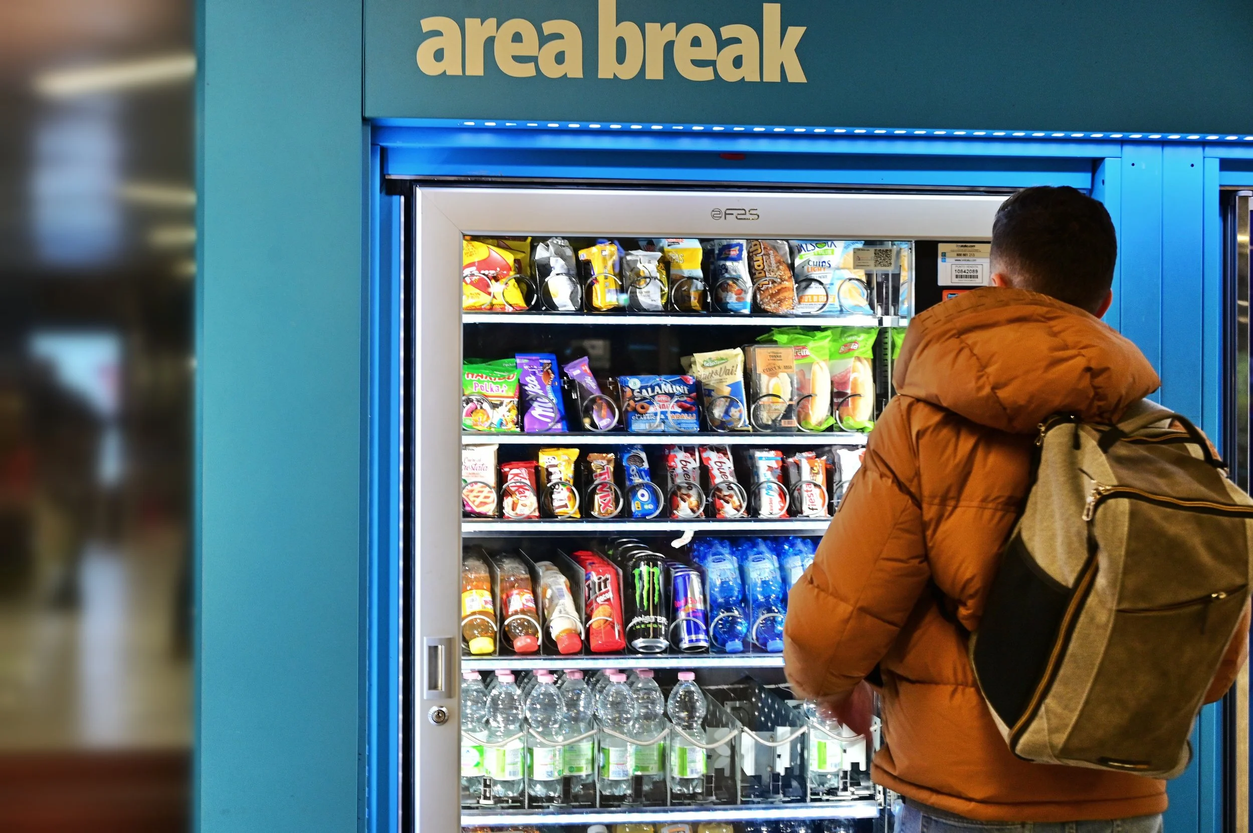A person with a backpack in front of a vending machine labeled 'area break' filled with snack and beverage options.