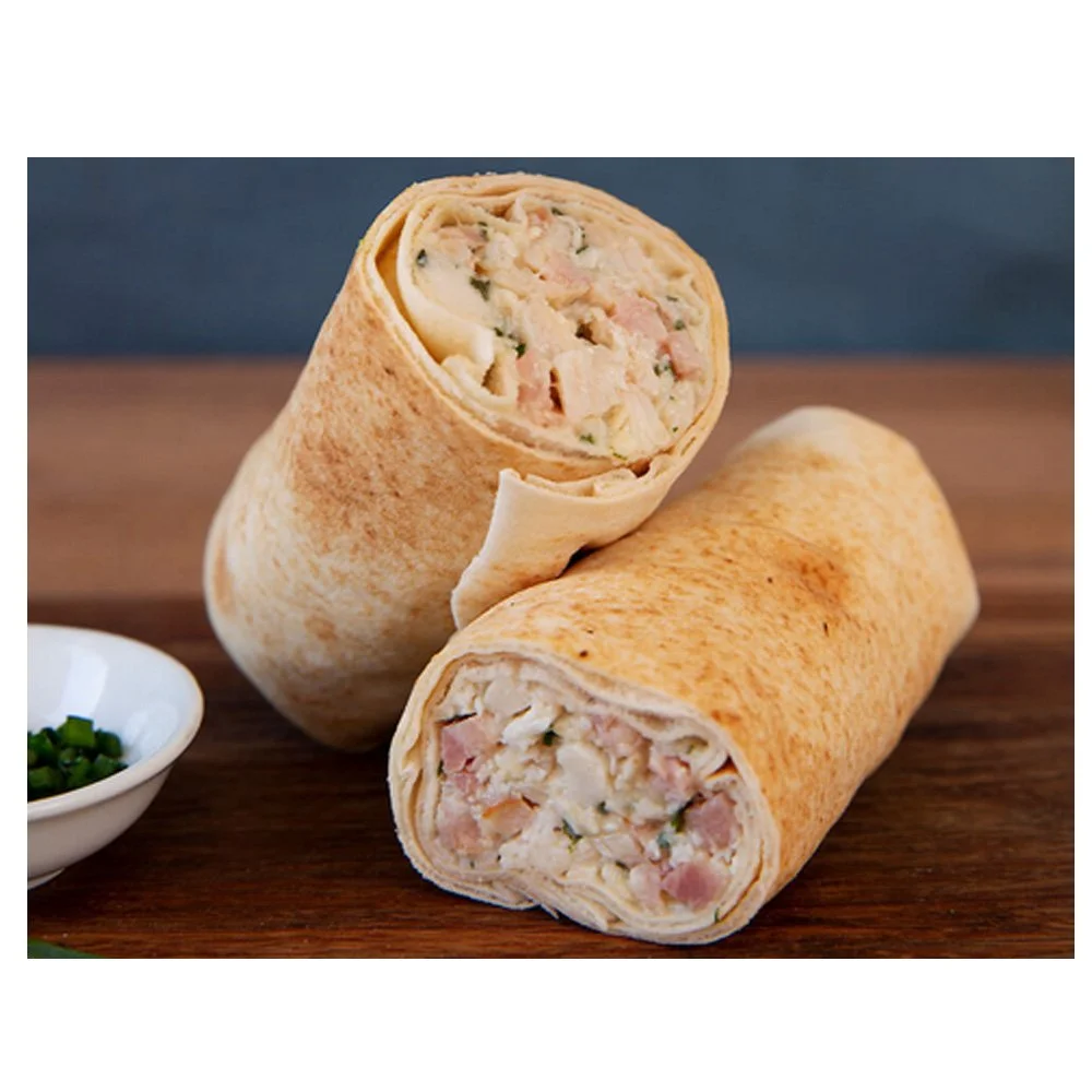 Two chicken Caesar wraps on a wooden surface with a small bowl of chopped green onions beside them.