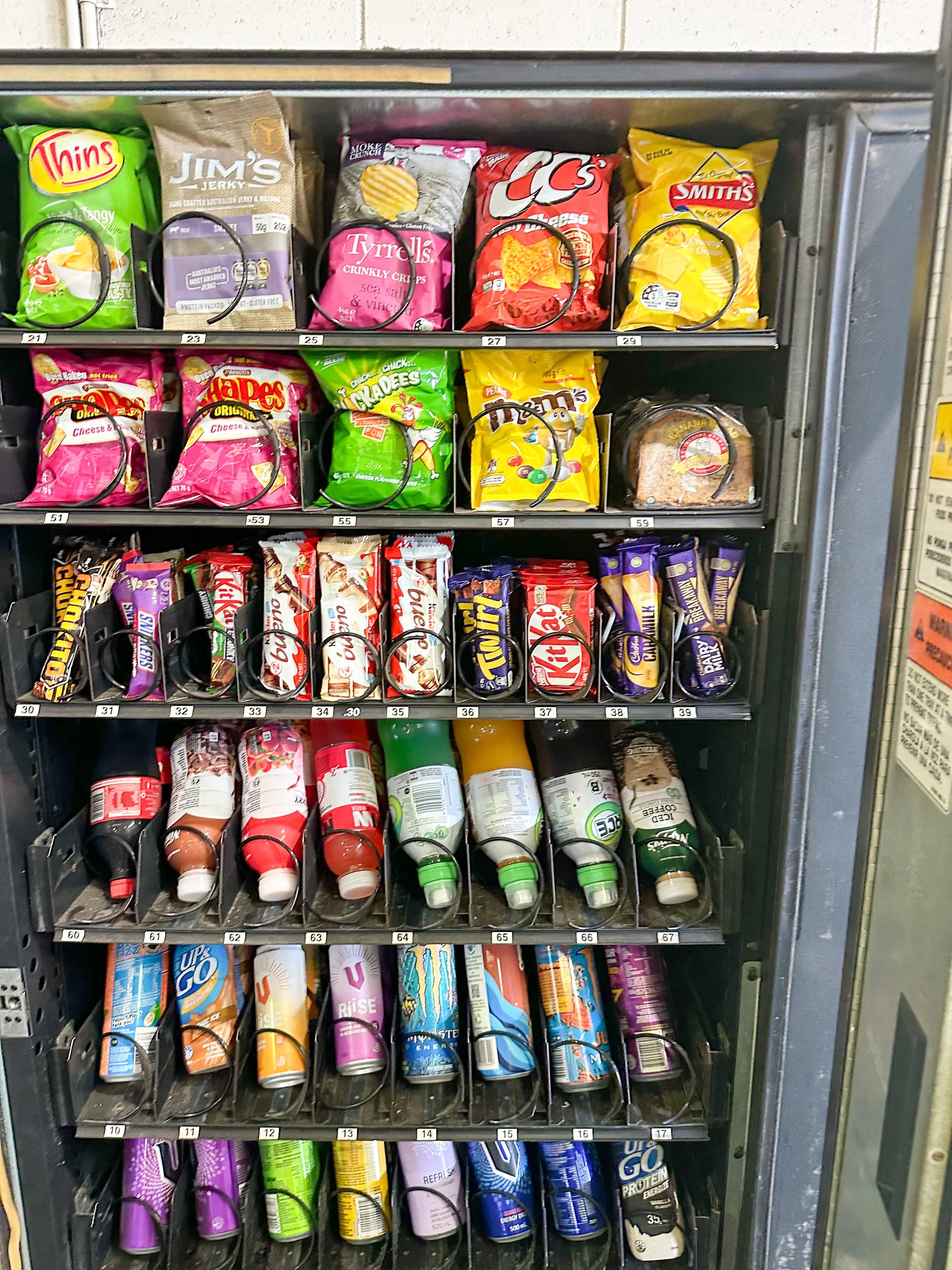 A vending machine stocked with various snack foods and beverages, including chips, candy bars, and bottled drinks.