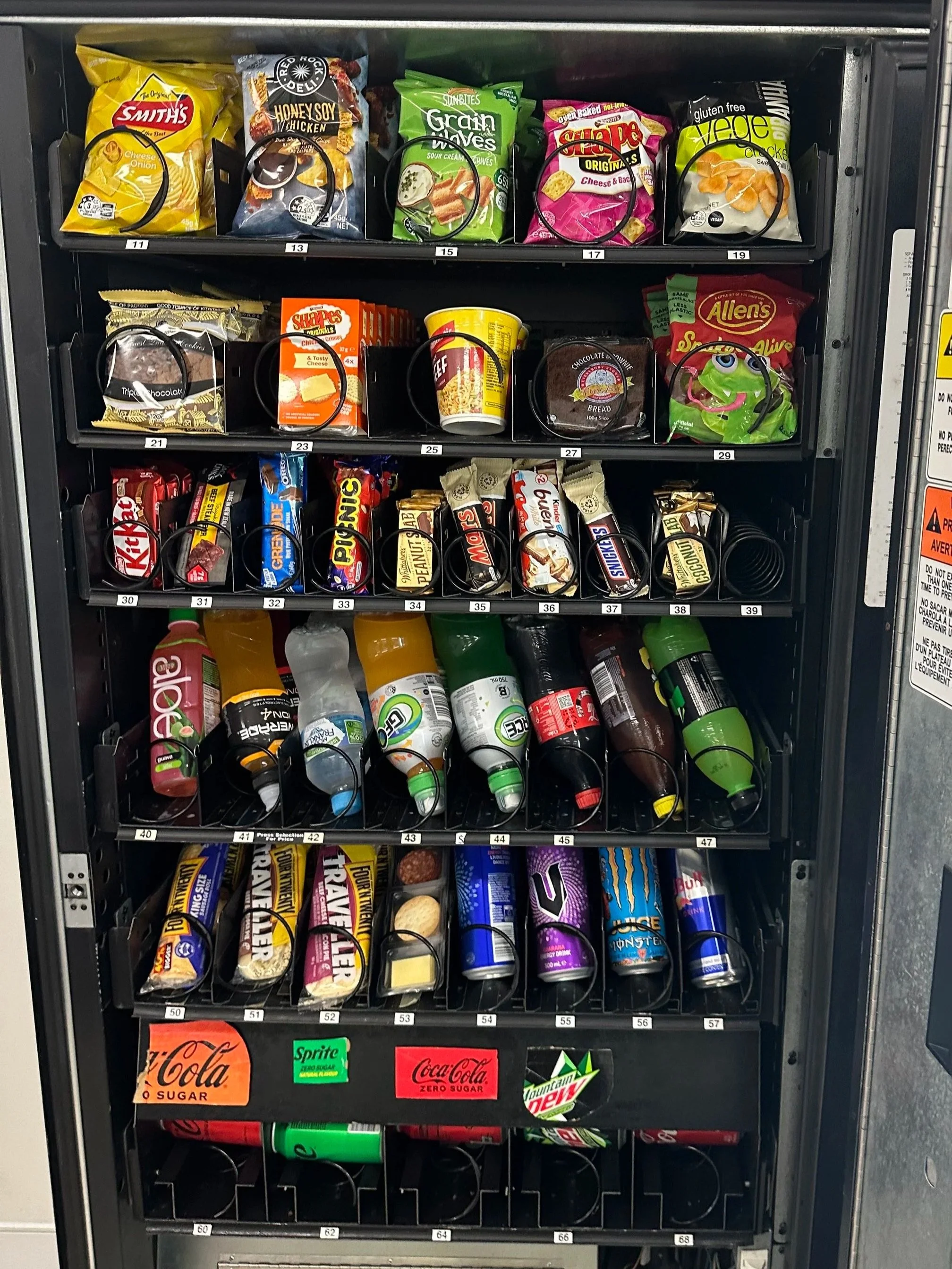 A vending machine stocked with snacks and drinks, including chips, candy, cookies, and bottled beverages.