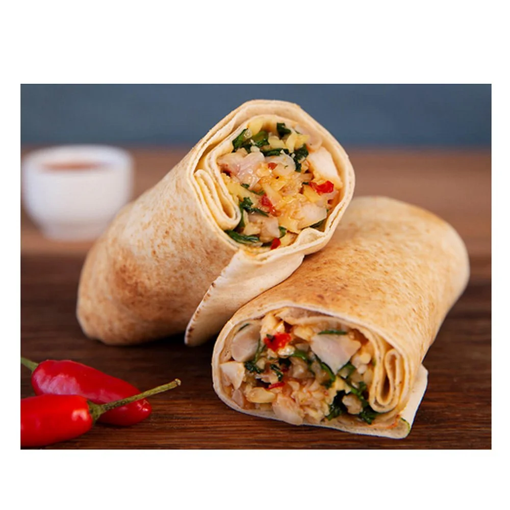 Two burritos filled with chicken, vegetables, and herbs on a wooden surface, with red chili peppers and a small container of sauce in the background.