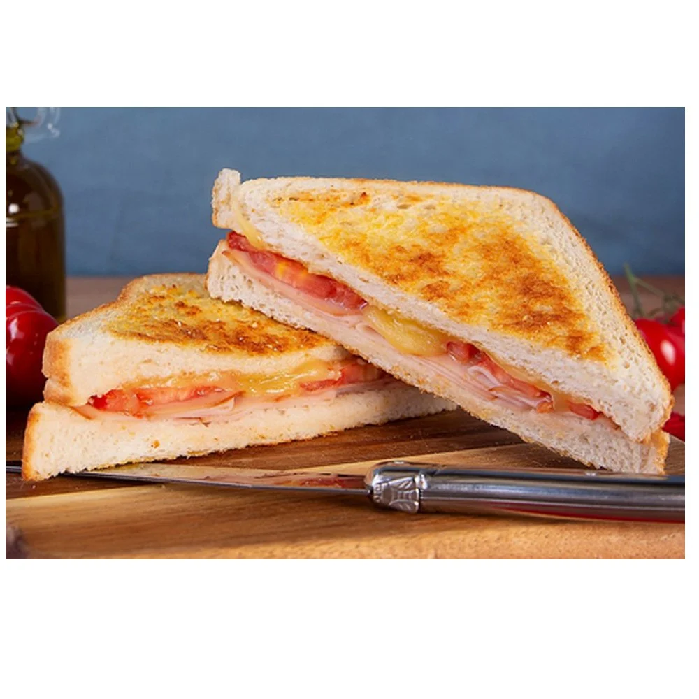 A grilled cheese sandwich with tomato and ham, cut diagonally in half, on a wooden cutting board with a butter knife.
