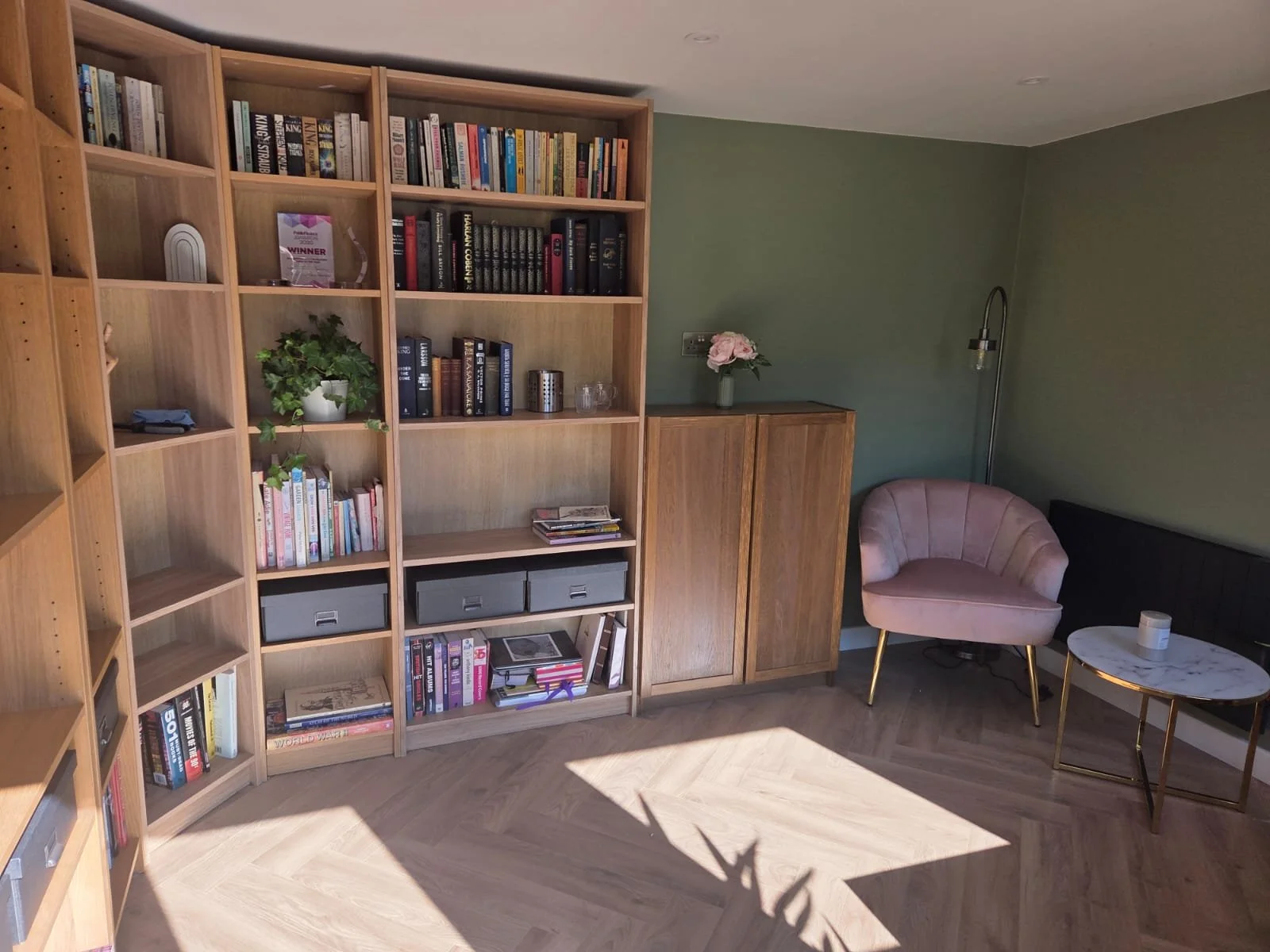 A garden reading room with fitted bookshelves, herringbone flooring and a quiet seating area.