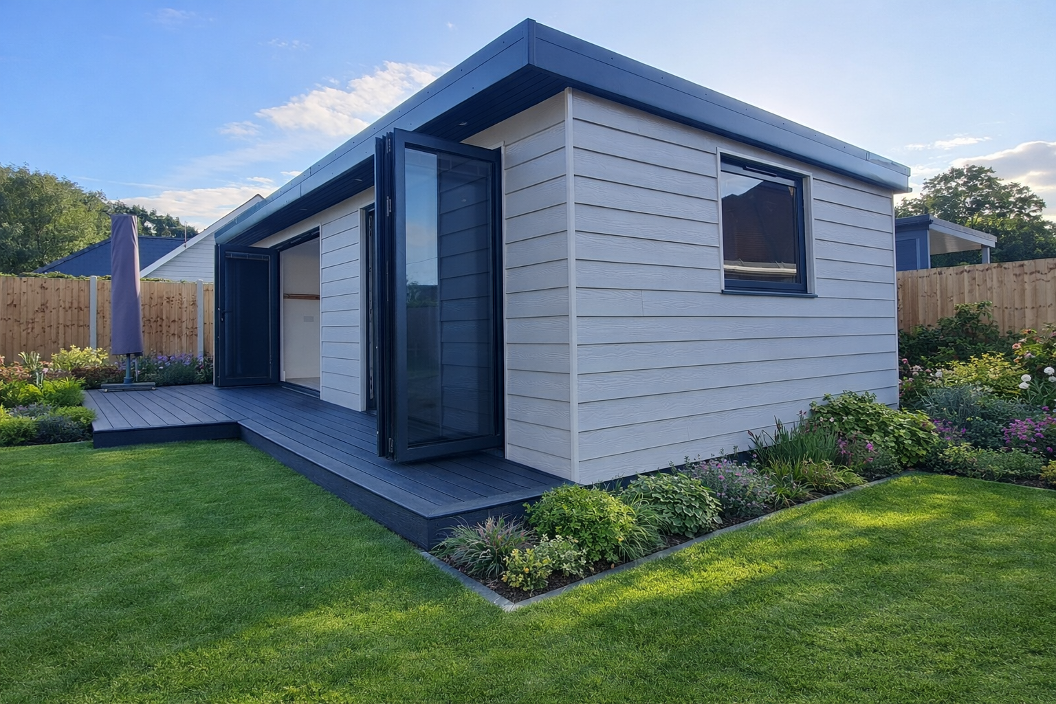 White garden room with bifold doors, composite decking and planted borders