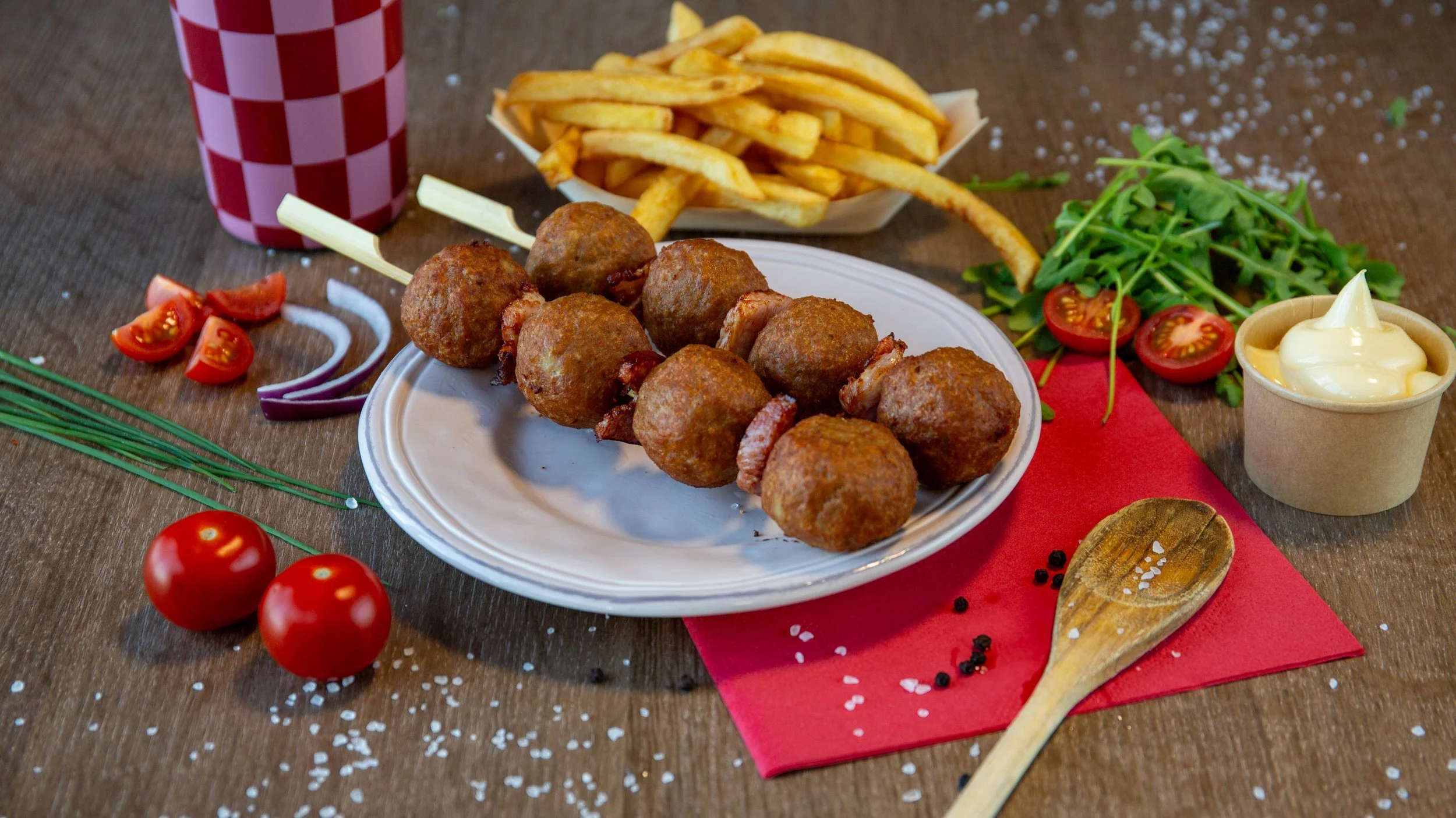 Gerechten met gehakte kroketten, frietjes, verse tomaten en salade op een houten tafel.
