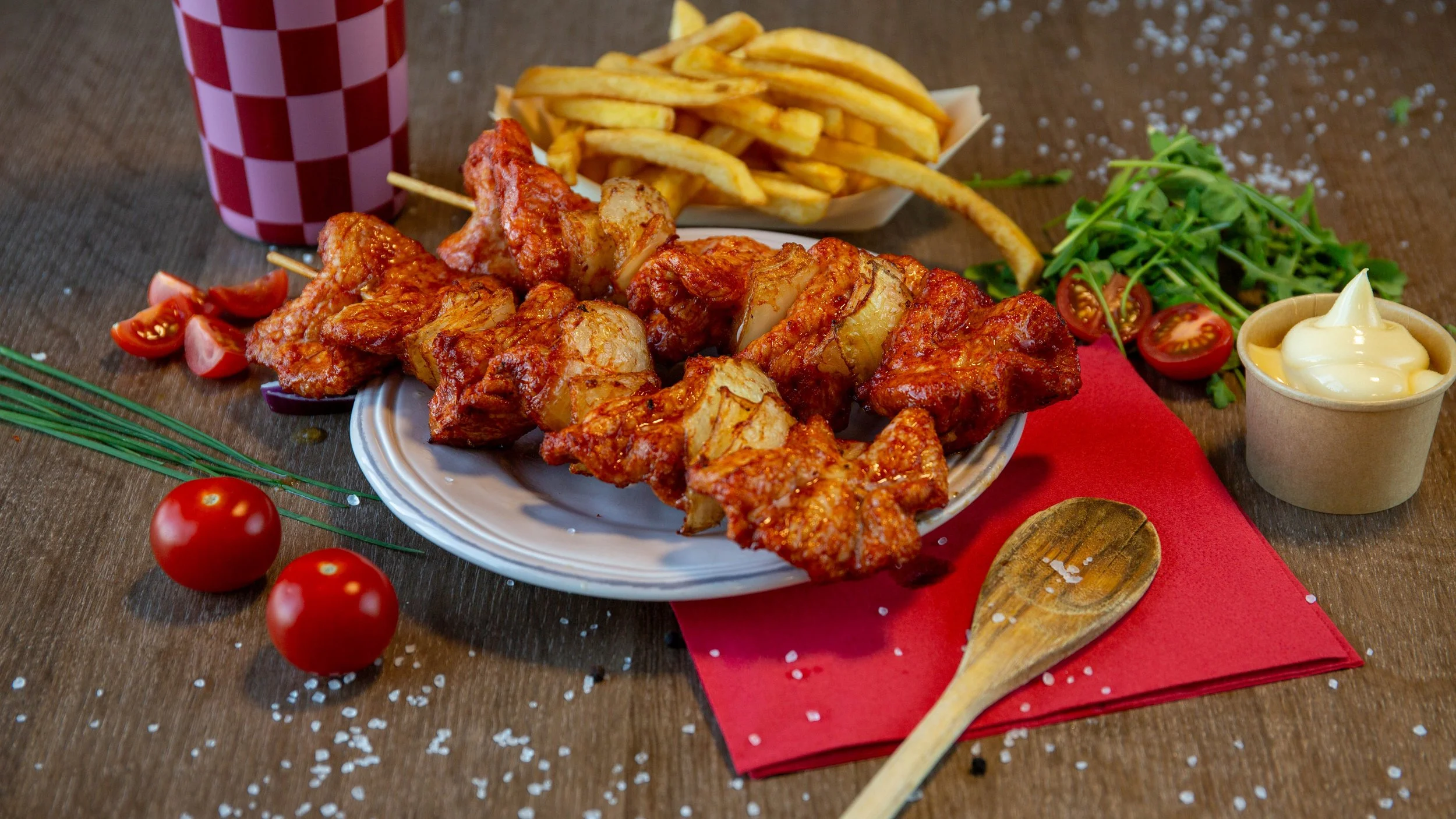 Gefrituurde kipvleugels met frietjes op een bord, met cherrytomaten, salade, Mayonaise in een cup, frisdrank, en decoratieve tomaten en cherrytomaten op de tafel.