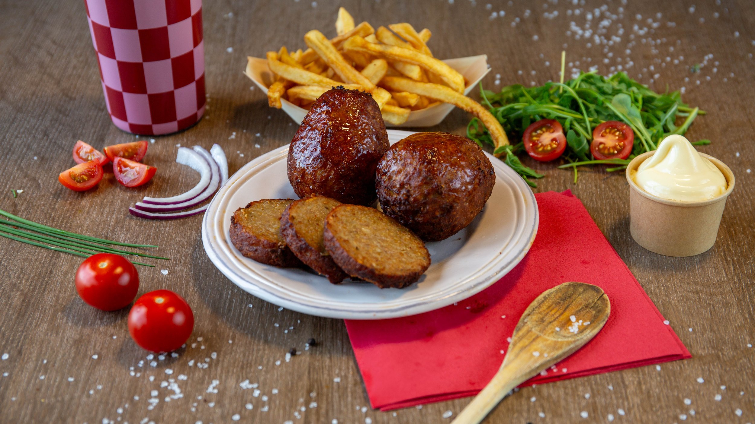 Bord met Gehaktballen, Franse frieten, salade met cherry tomaten en rucola, gehaktballetjes met saus, en een glas frisdrank