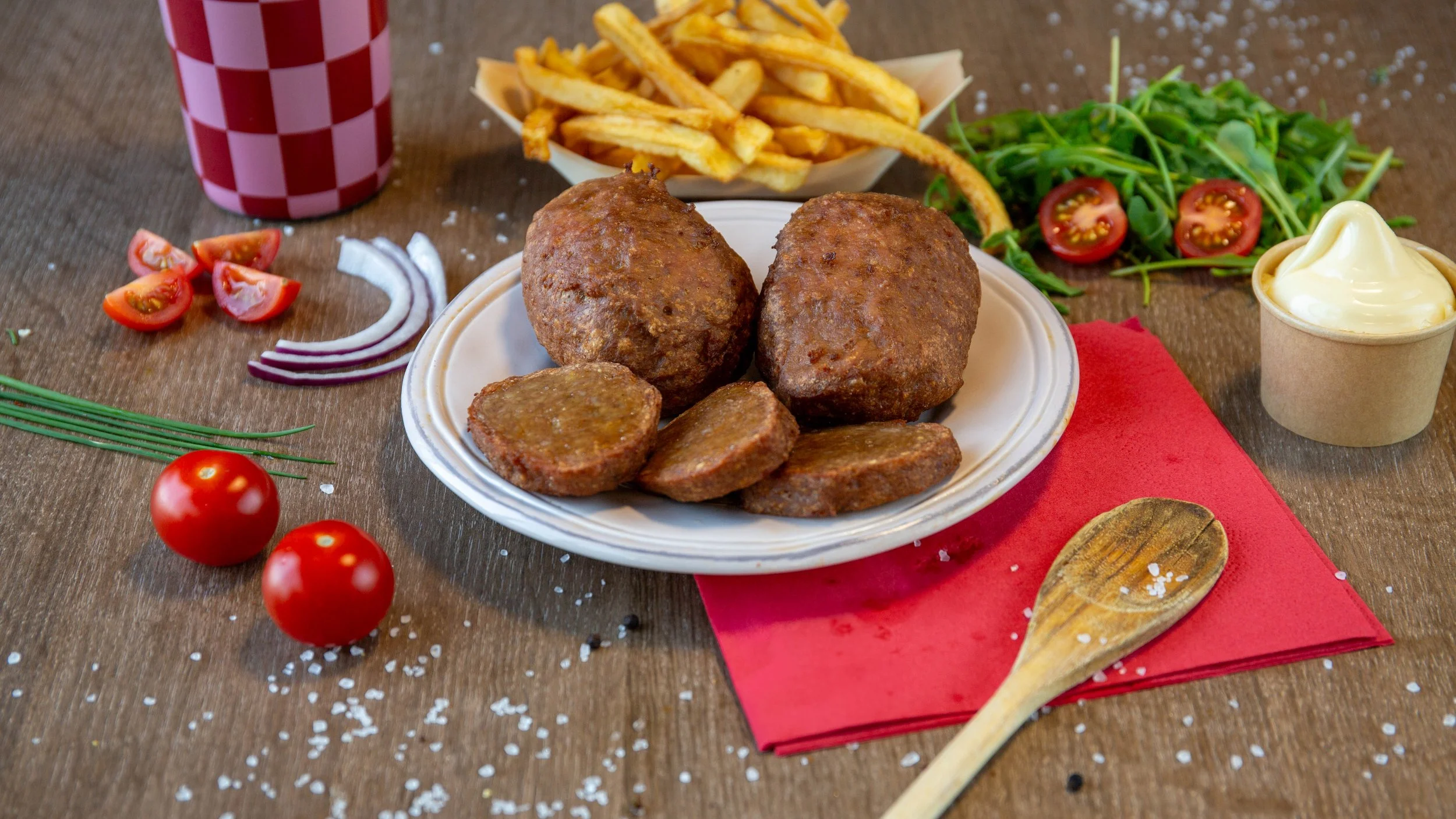 Bord met Zweedse köttbullar, frieten, salade, ketchup, mayonaise en cherrytomaten.