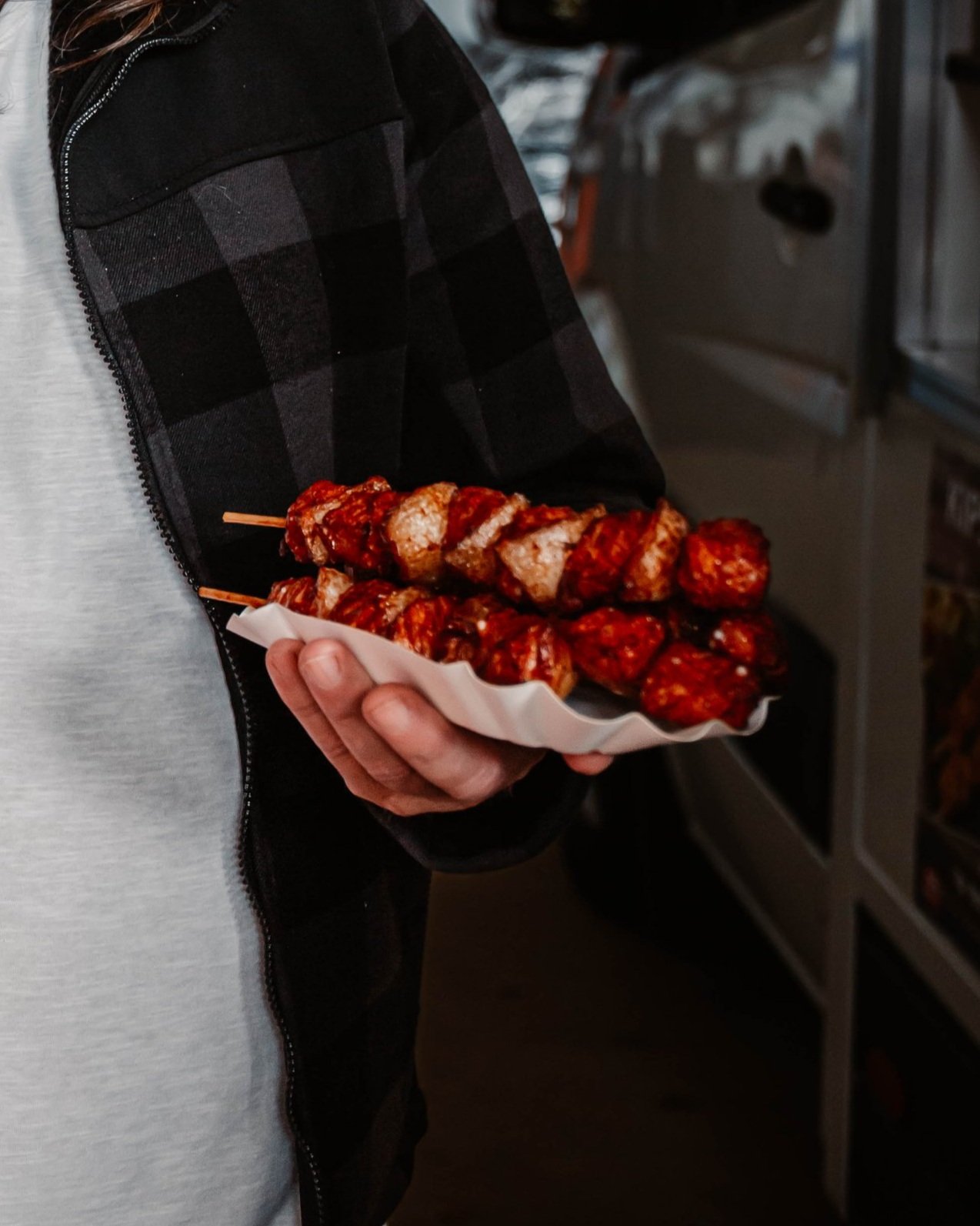 Een persoon houdt een dienblad met lopende vleesspiezen in de hand.