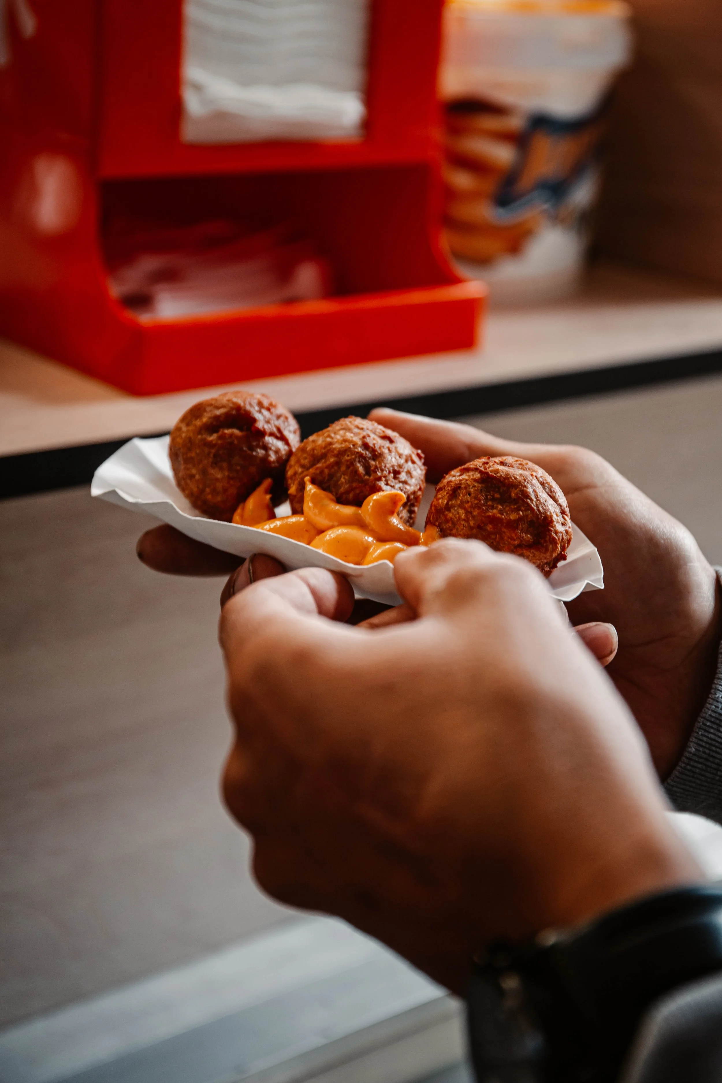 Persoon houdt een papieren bord met drie gehaktballen en gekaramelliseerde uien.