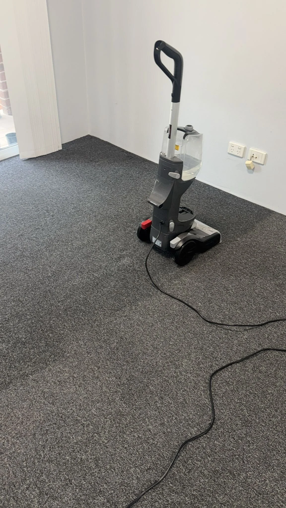A vacuum cleaner on a gray carpeted floor near a white wall with electrical outlets.