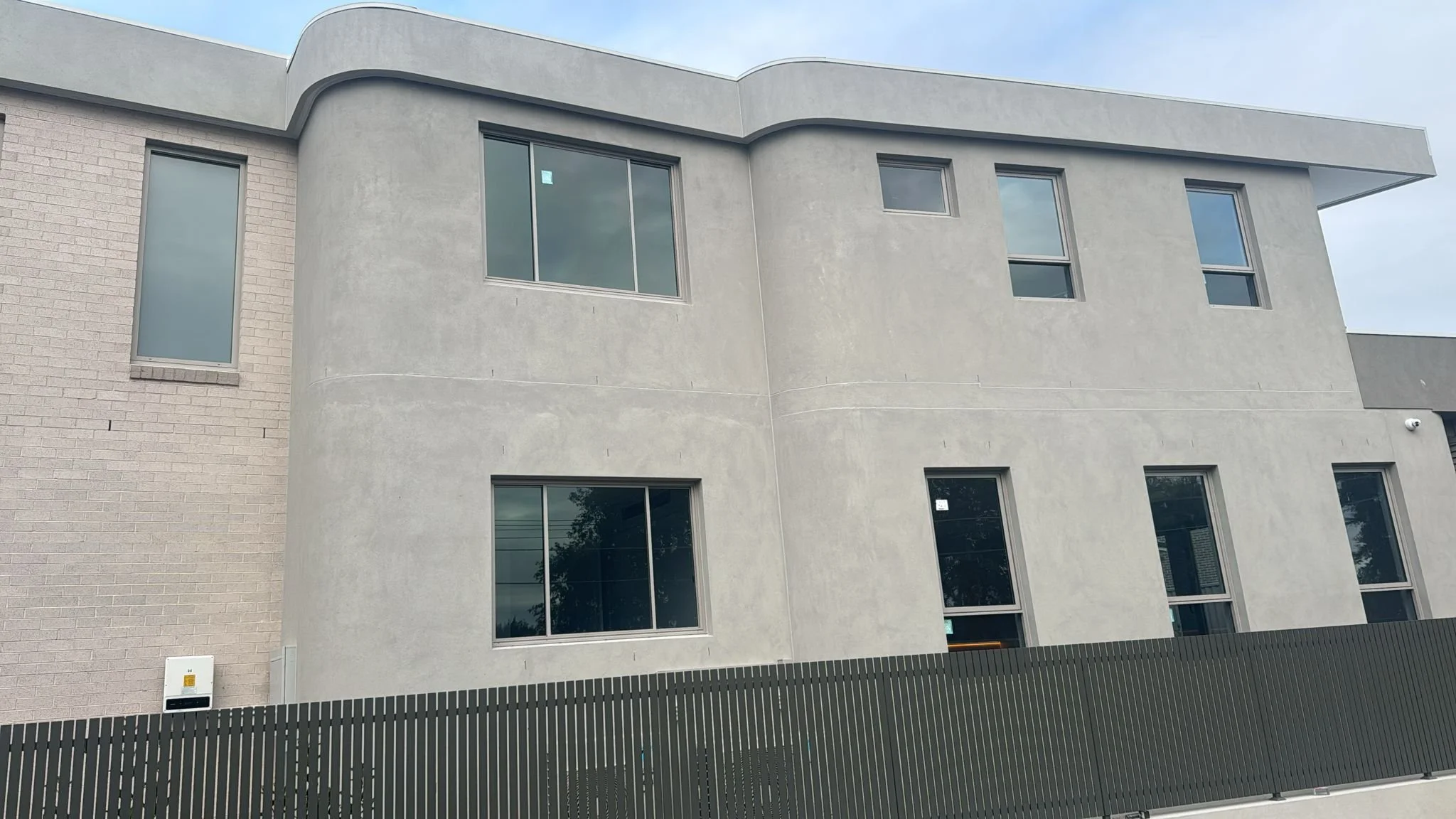 Modern multi-story residential building with large windows and a dark fence in front.