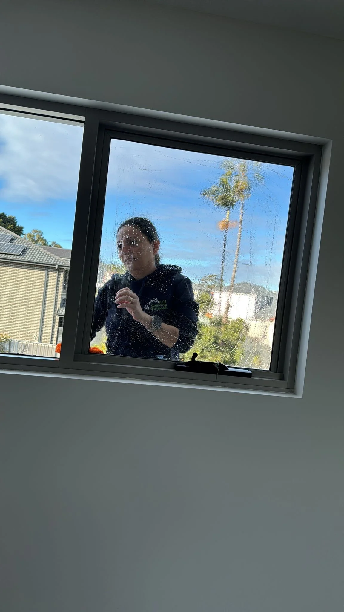 Person looking through a foggy window with water droplets, outdoors with a cloudy sky and palm trees in the background.