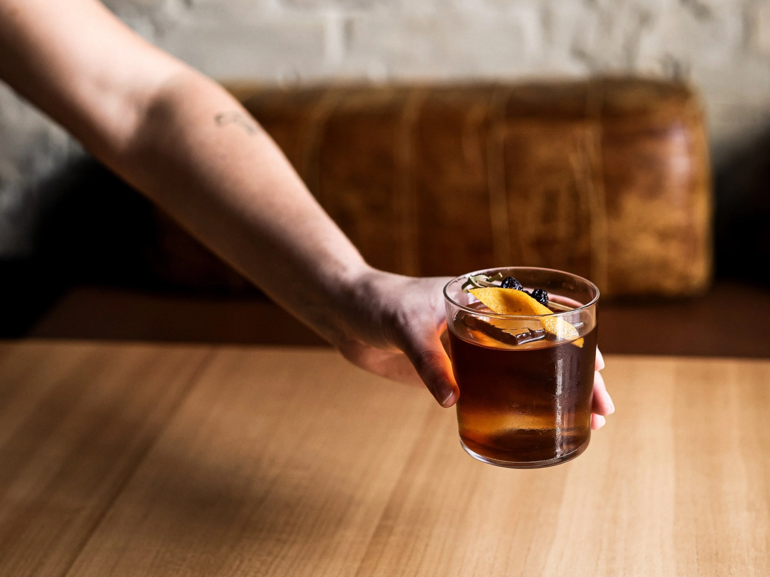 Hånd, der tilsætter en skive agurk i et glas med farverigt cocktail.