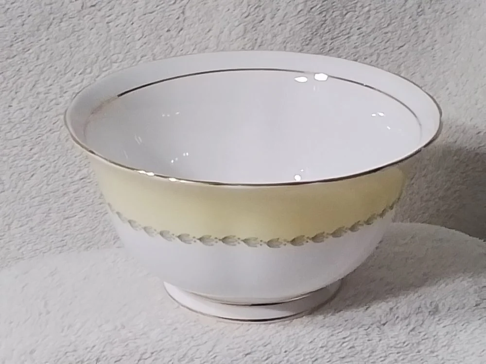 A white ceramic bowl with a decorative yellow band and scalloped design, sitting on a textured white surface.