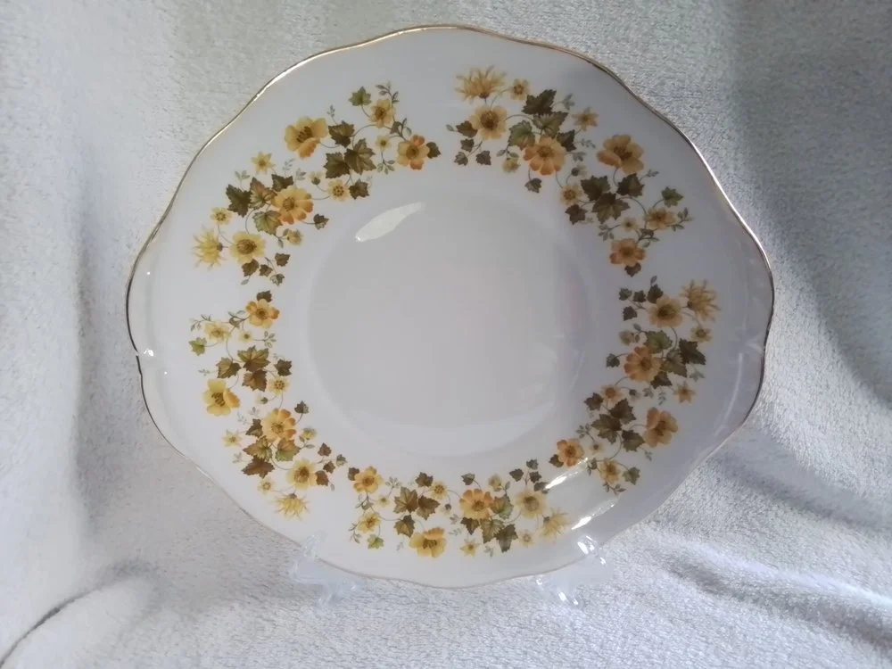 A white porcelain plate with a gold scalloped edge and a floral pattern of yellow and orange flowers with green leaves around the rim.