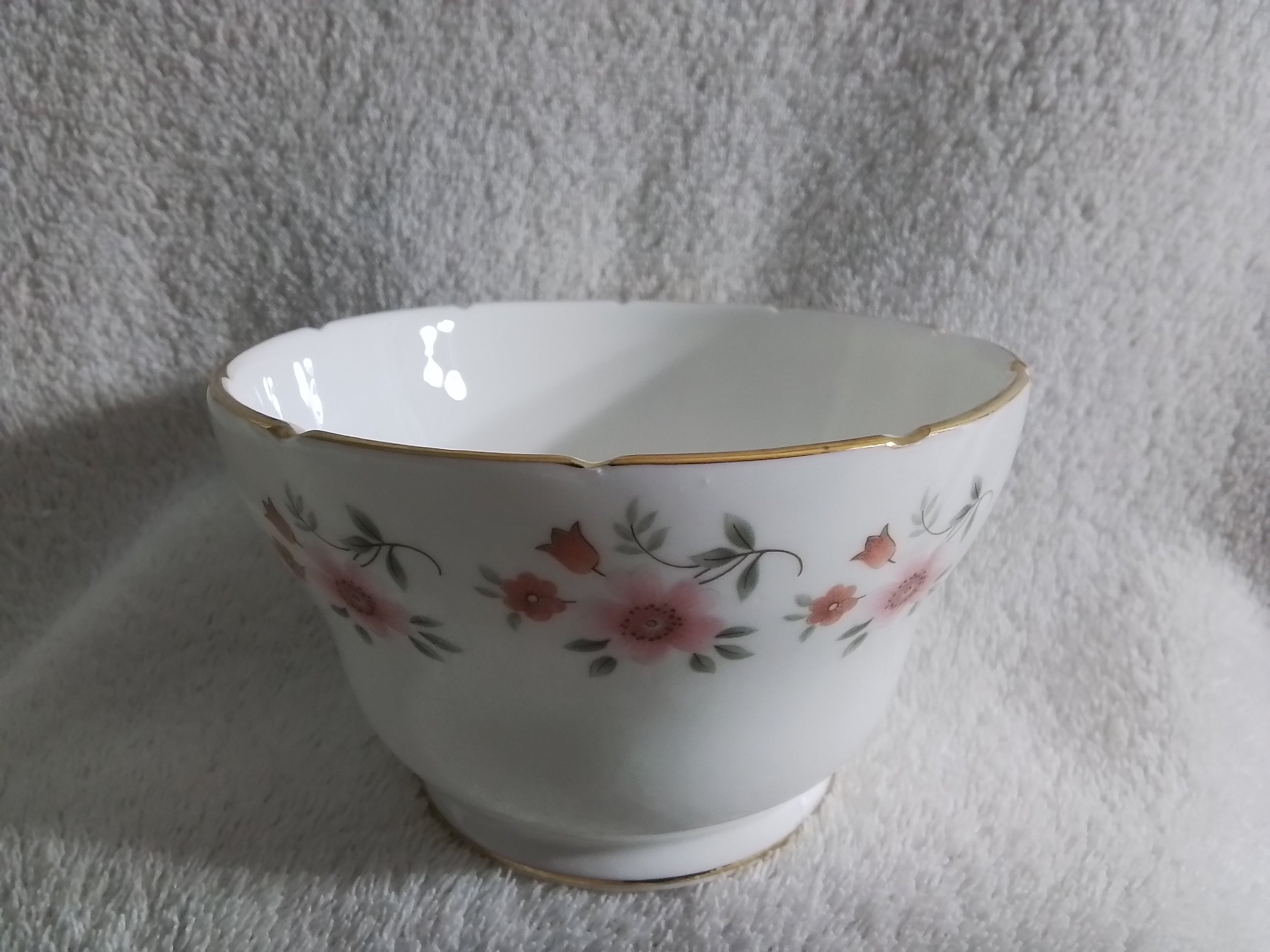 A white porcelain bowl with pink and green floral design and gold trim, placed on a textured white surface.