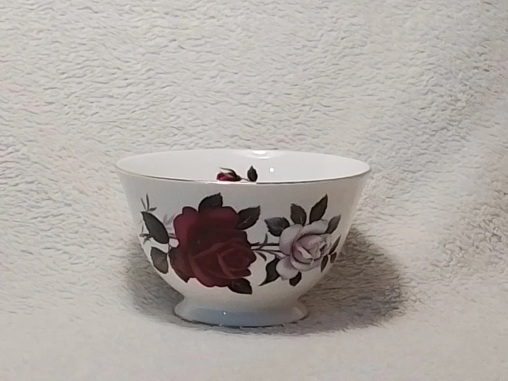 A white ceramic bowl with a rose floral pattern, containing some small remnants of what was likely food or a snack, placed on a textured light-colored surface.