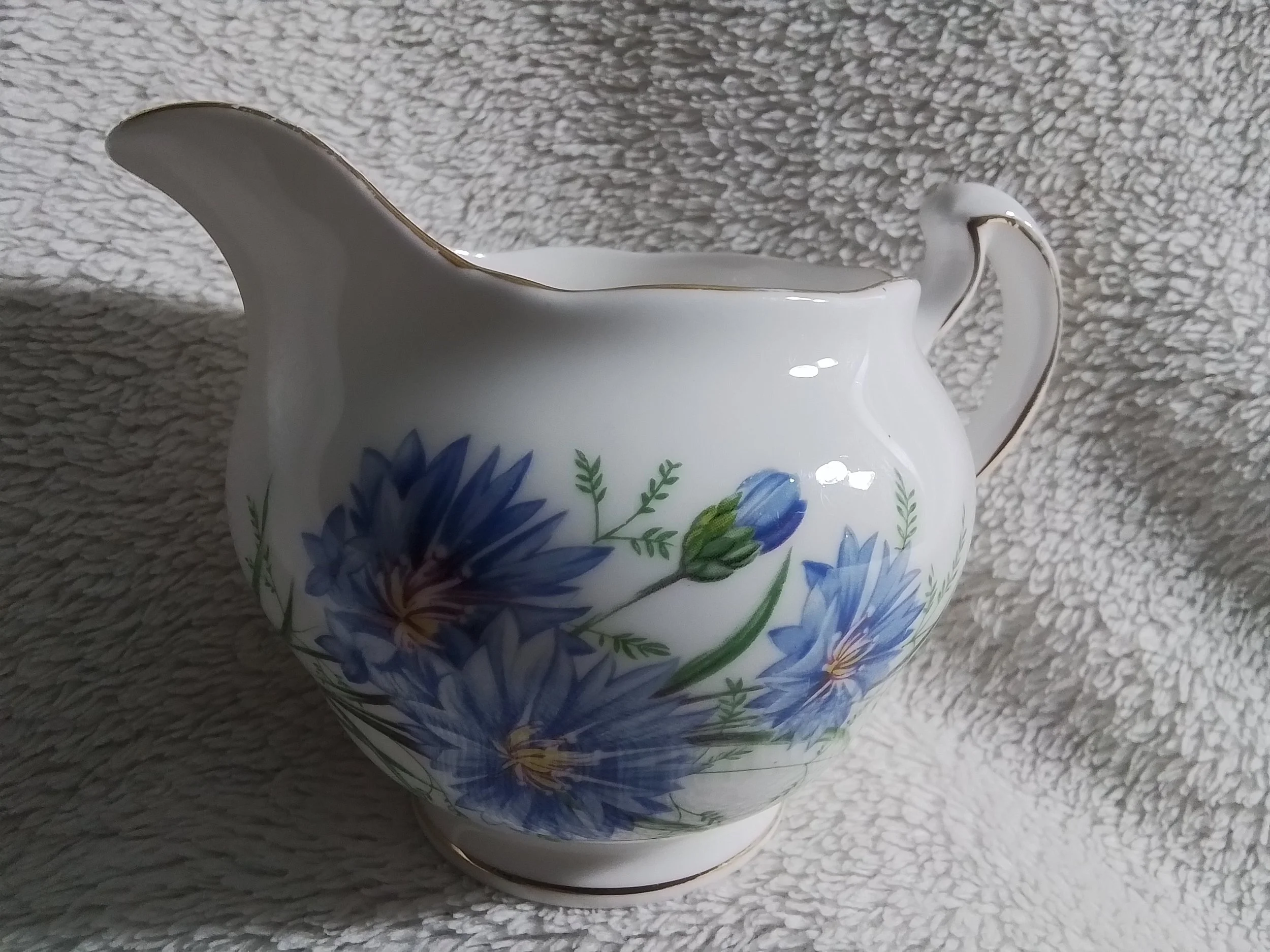 A white porcelain pitcher with blue floral patterns and gold accents, placed on a textured light gray surface.