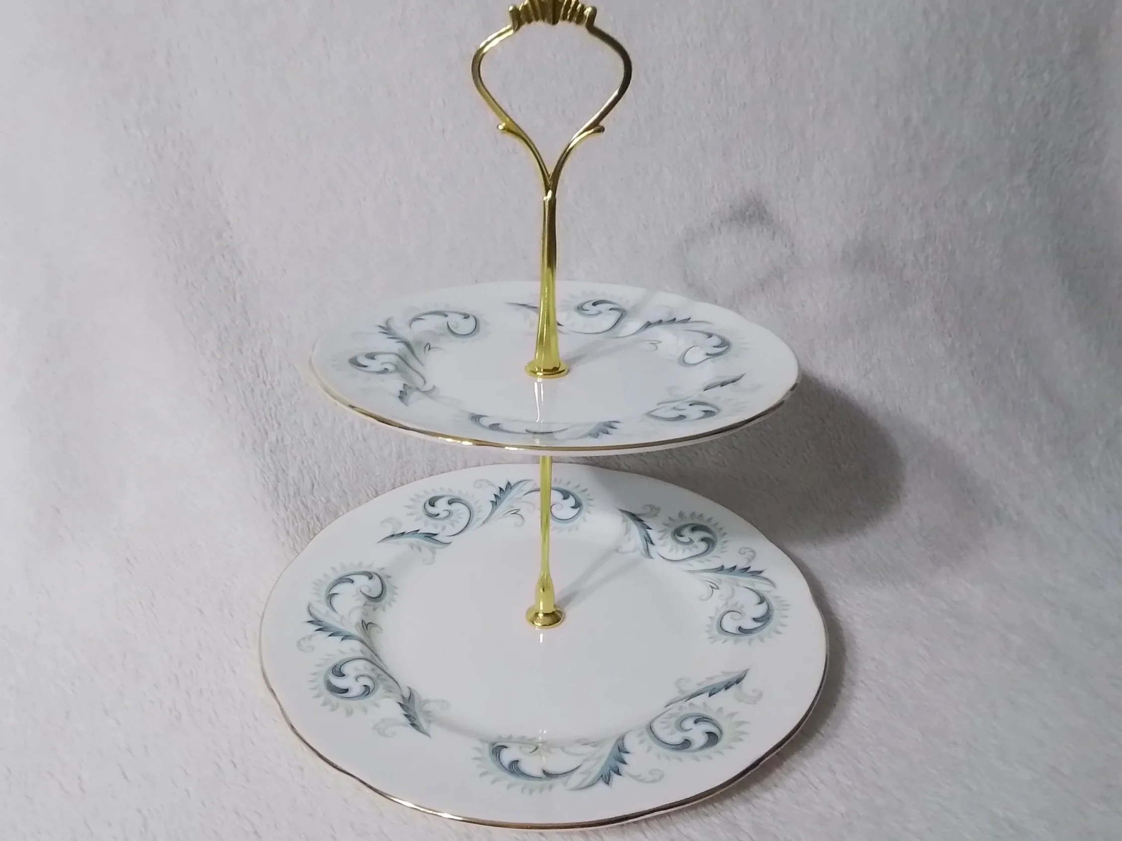 Two-tiered decorative ceramic serving stand with gold accents and floral patterns, against a plain white background.