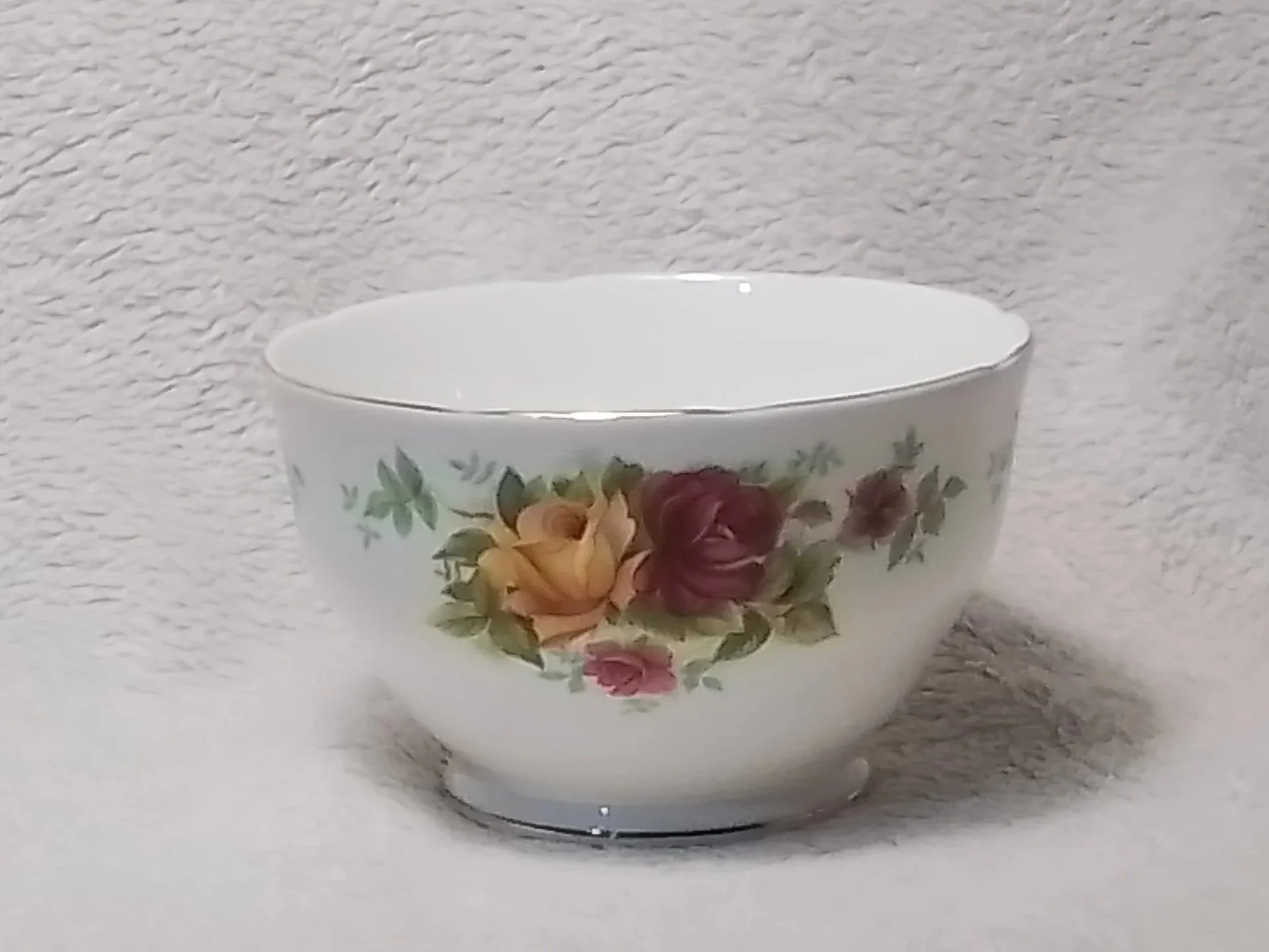White porcelain bowl with floral pattern of roses and green leaves, placed on a textured light-colored surface.