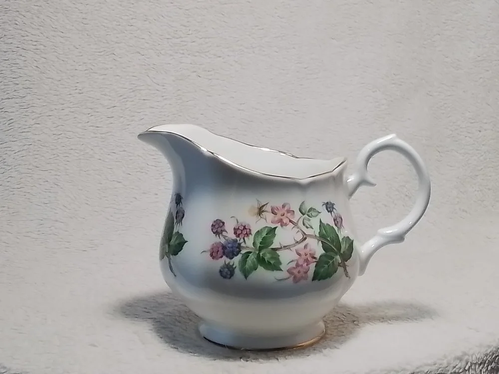 A white porcelain creamer with floral pattern featuring pink, purple, and green leaves.