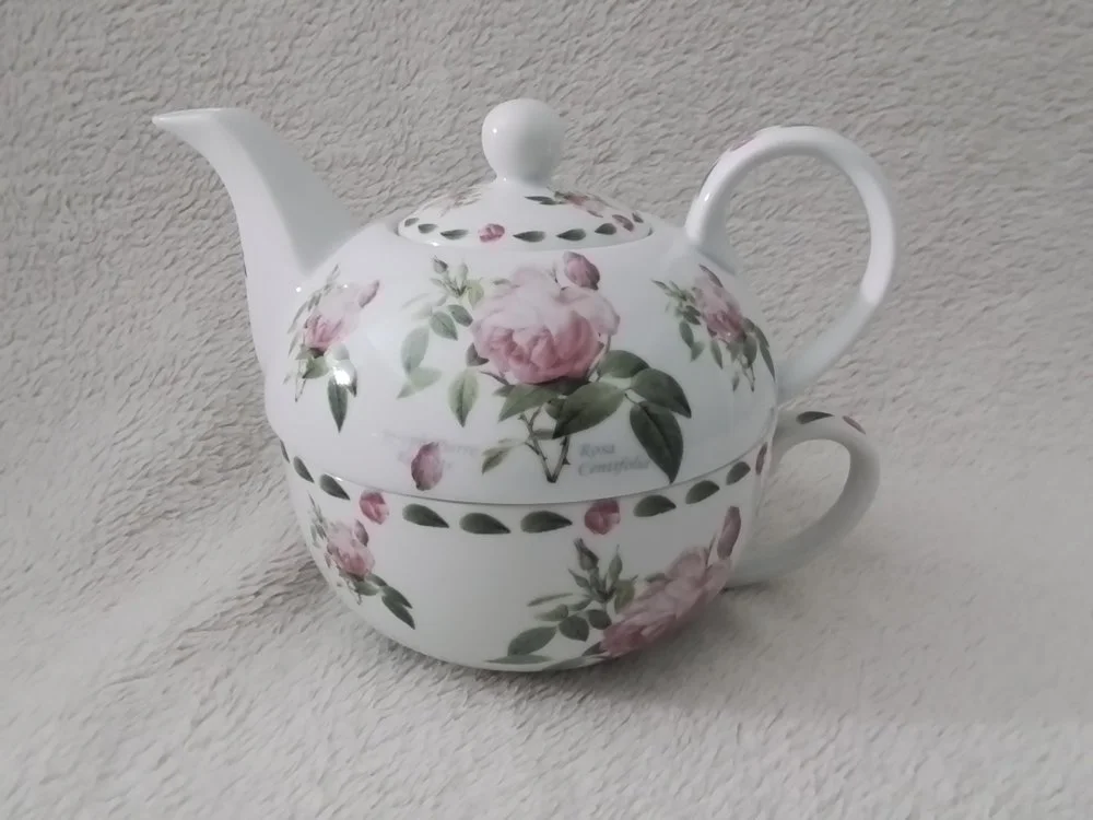 A teapot with a floral pink rose and green leaf pattern.