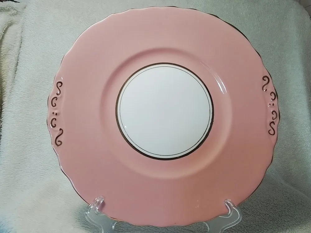 Pink decorative plate with a floral pattern on the edges displayed on a clear stand.