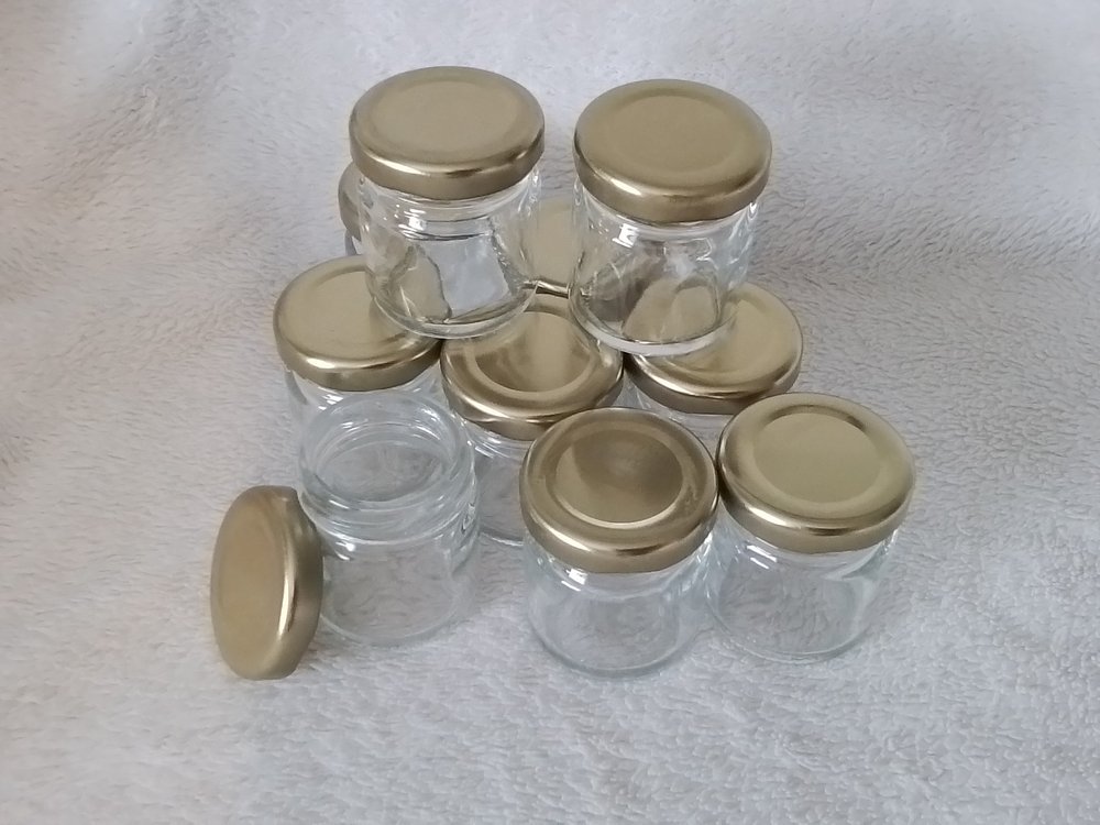 A group of small empty glass jars with gold-colored metal lids on a light-colored textured surface.