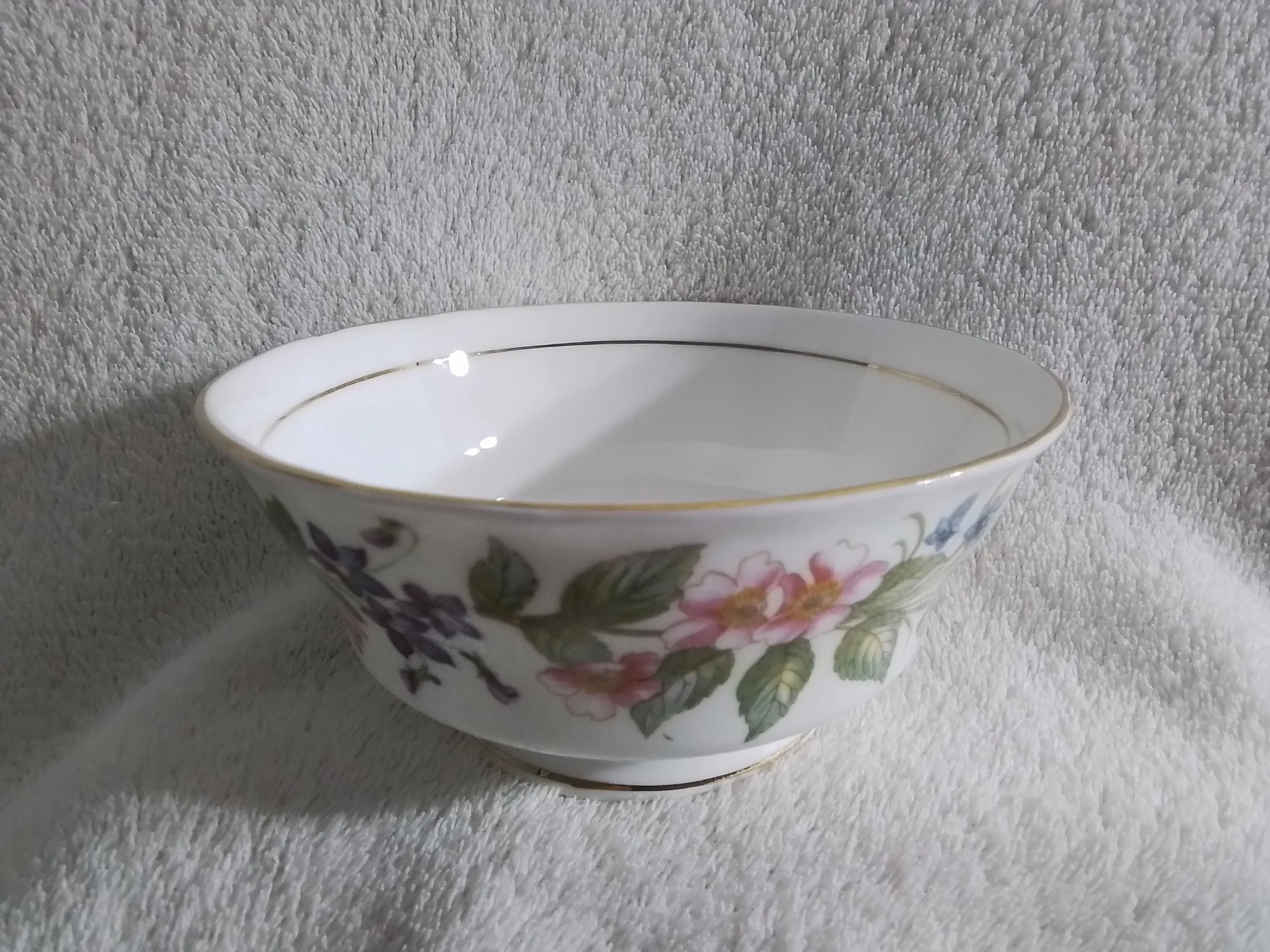 A white porcelain bowl with gold trim and floral designs, placed on a textured beige fabric background.